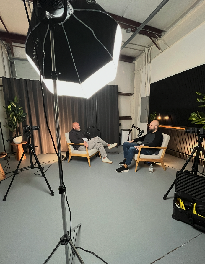 Two men recording a podcast in a studio with microphones, cameras, and softbox lighting
