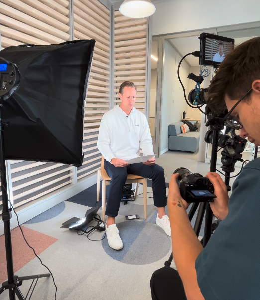 Video production setup with a seated man being filmed by a camera operator in a modern office