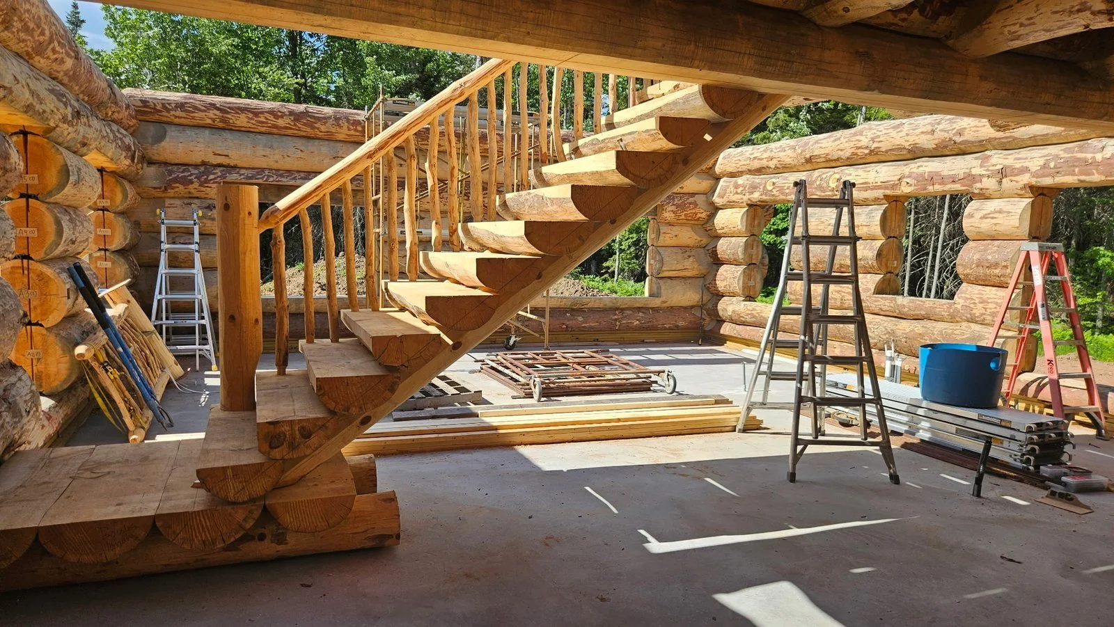 Custom log staircase with thick wooden treads and branch balusters inside a log home under construction.