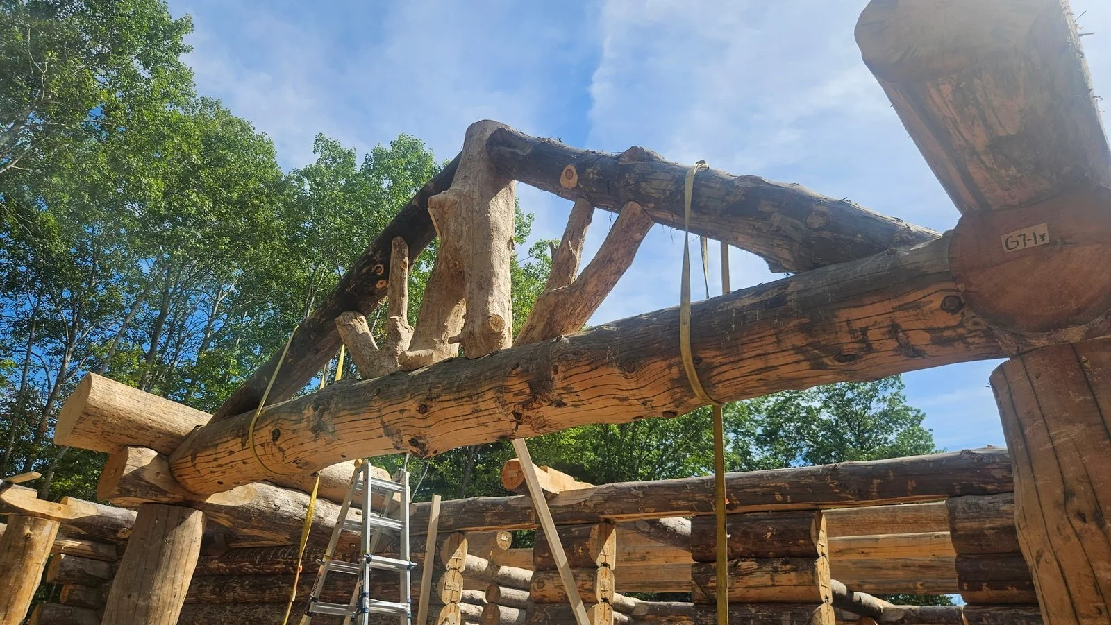 Handcrafted log roof truss with fitted joints and lifting straps during assembly.