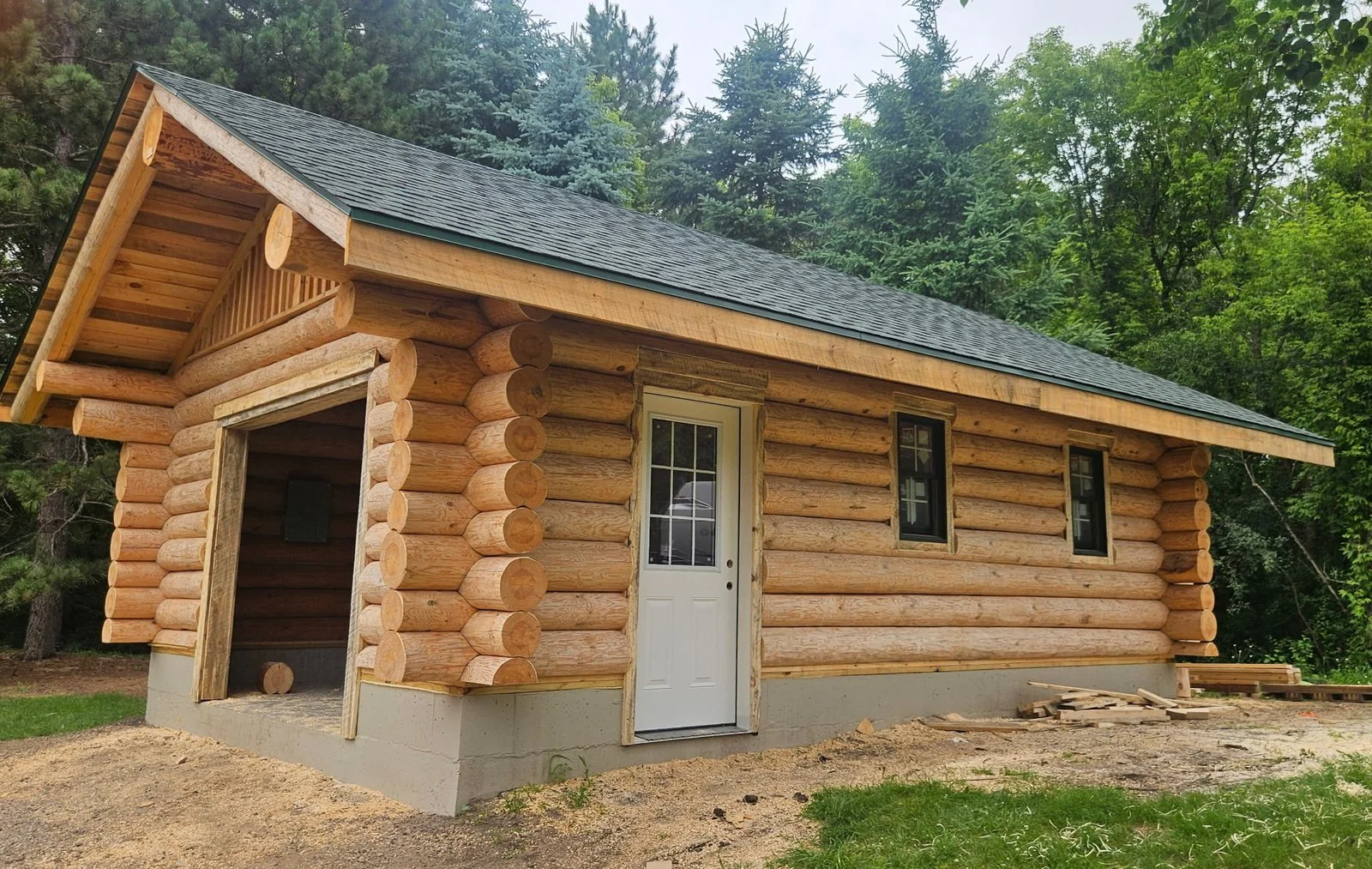Handcrafted log building with a shingled gable roof, fitted corner logs, and installed windows.