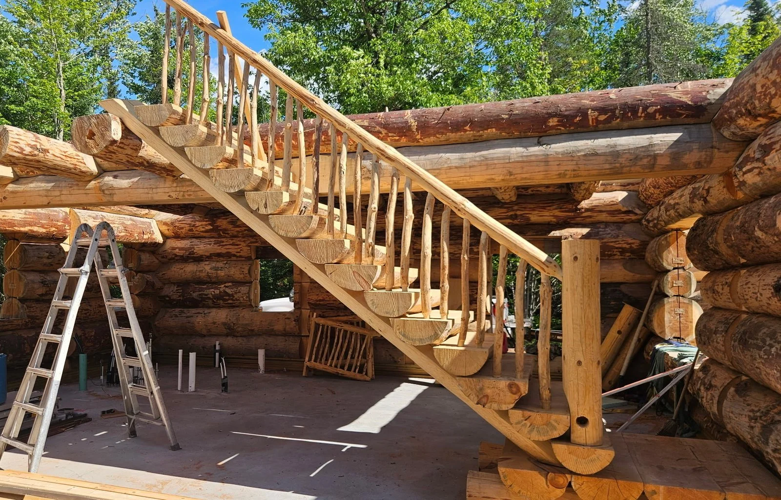 Log staircase with rounded timber treads, natural branch balusters, and a large support post.