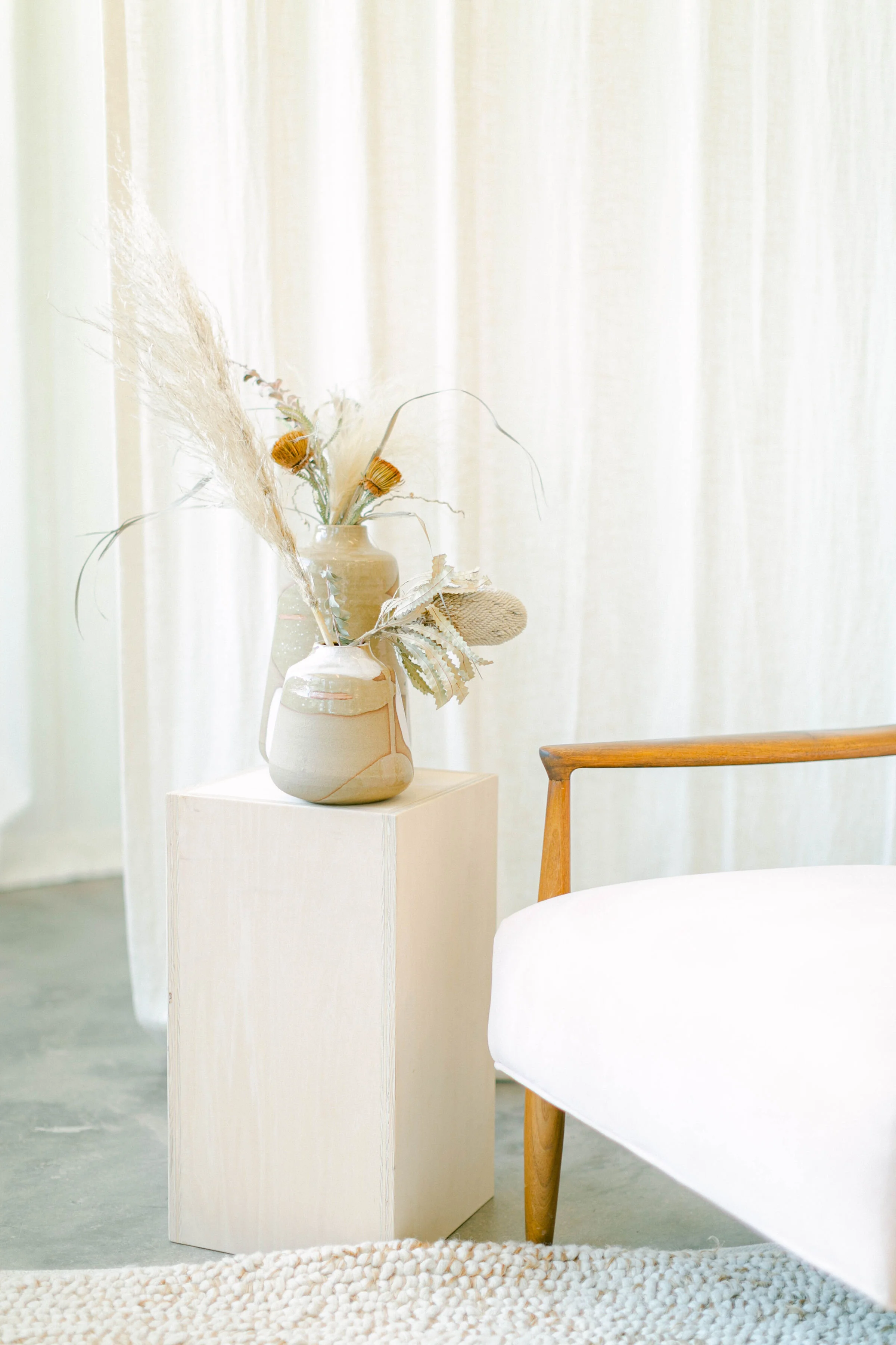 A cream chair with wood arms positioned by a side table with dried florals, offering a supportive space for exploring different internal parts during IFS-informed therapy in Denver.