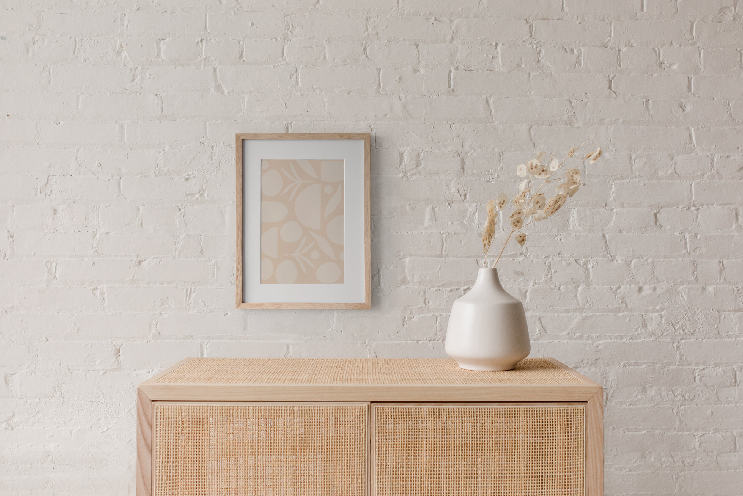 A framed CZTG brand pattern print hanging on a white painted brick wall above a tan piece of furniture.