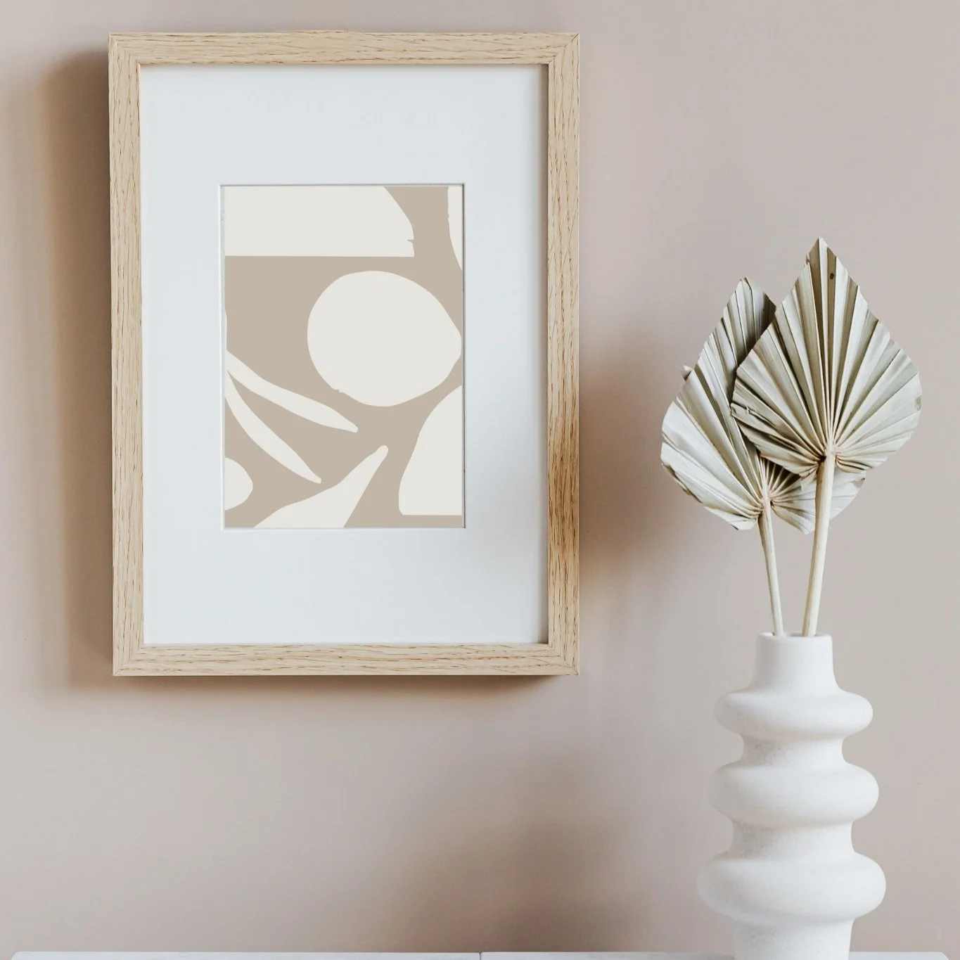 A framed CZTG brand pattern print displayed next to a white ceramic vase containing a dried fan palm leaf.
