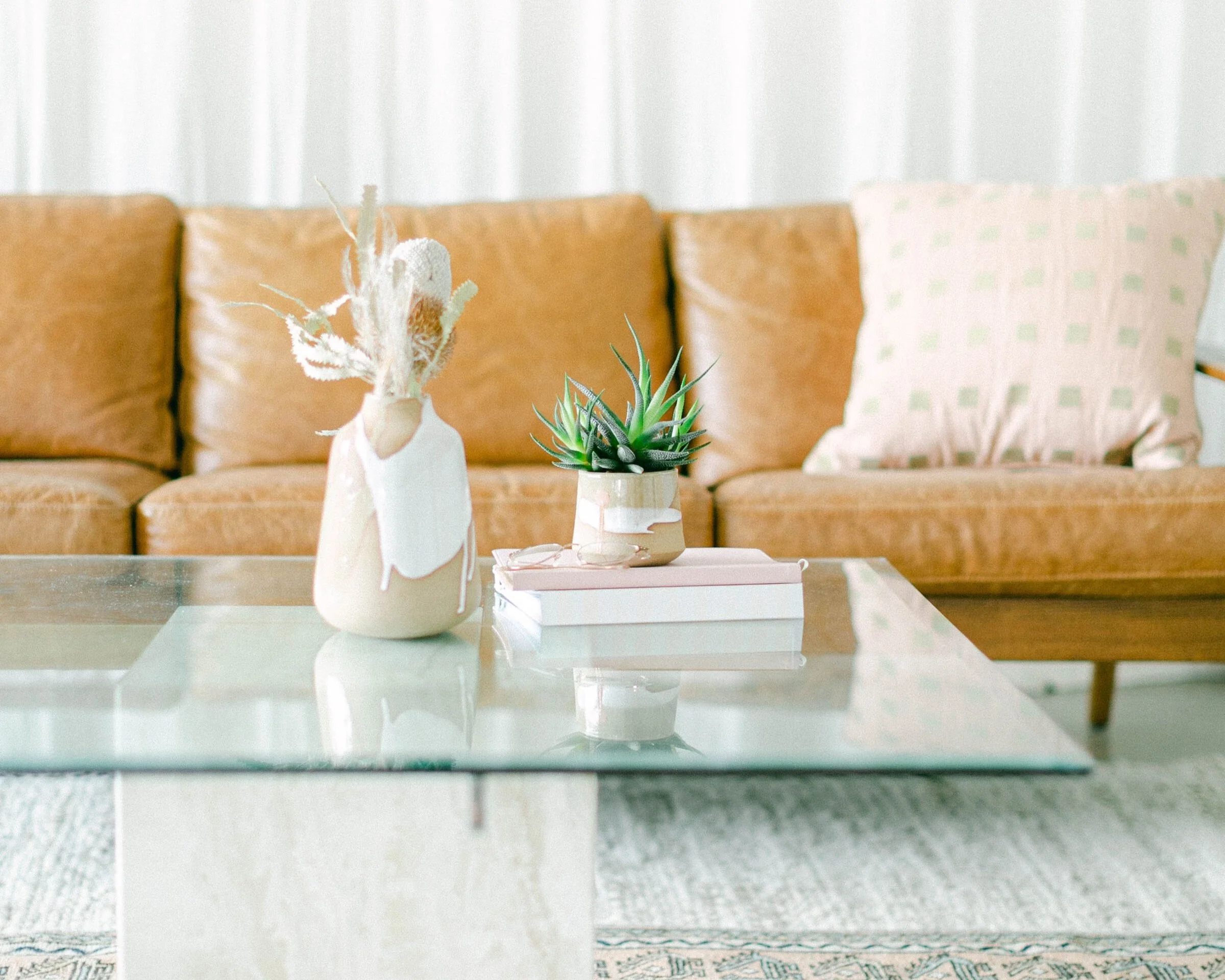 A modern camel-colored leather couch paired with a sleek glass coffee table in a bright, inviting room.