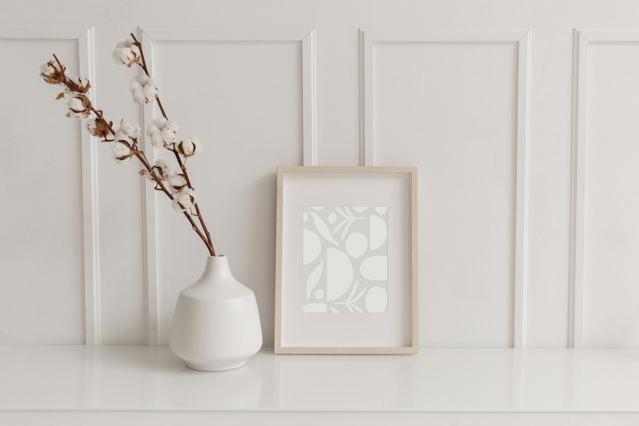 A framed CZTG botanical plant pattern print sitting next to a minimalist vase holding a floral tree branch.