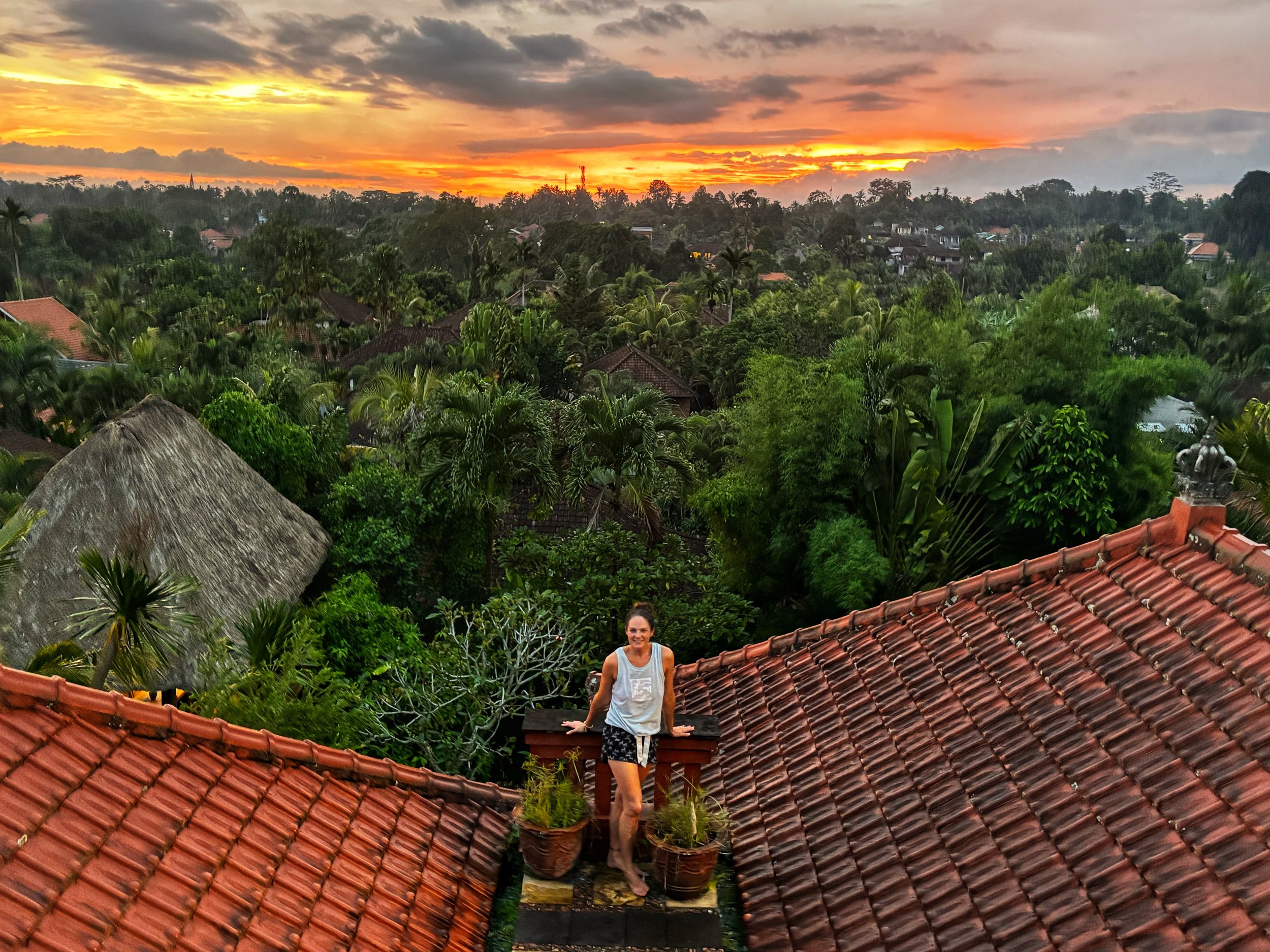 Lisa Kern traveling in Indonesia, surrounded by tropical greenery and rooftops beneath a vibrant sunset.