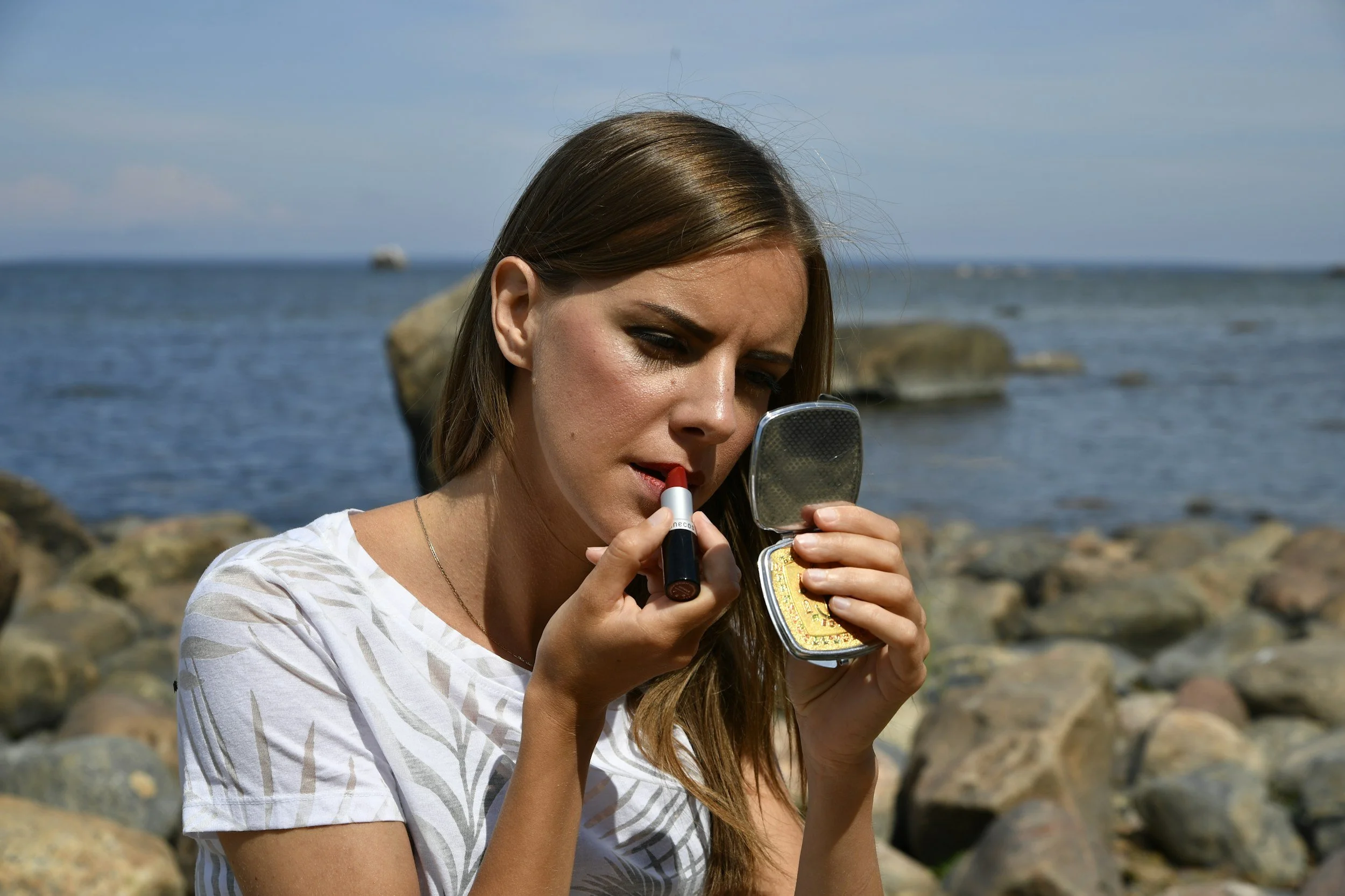 Woman looking at her reflection applying lipstick while reflecting on unrealistic beauty standards and social media pressure