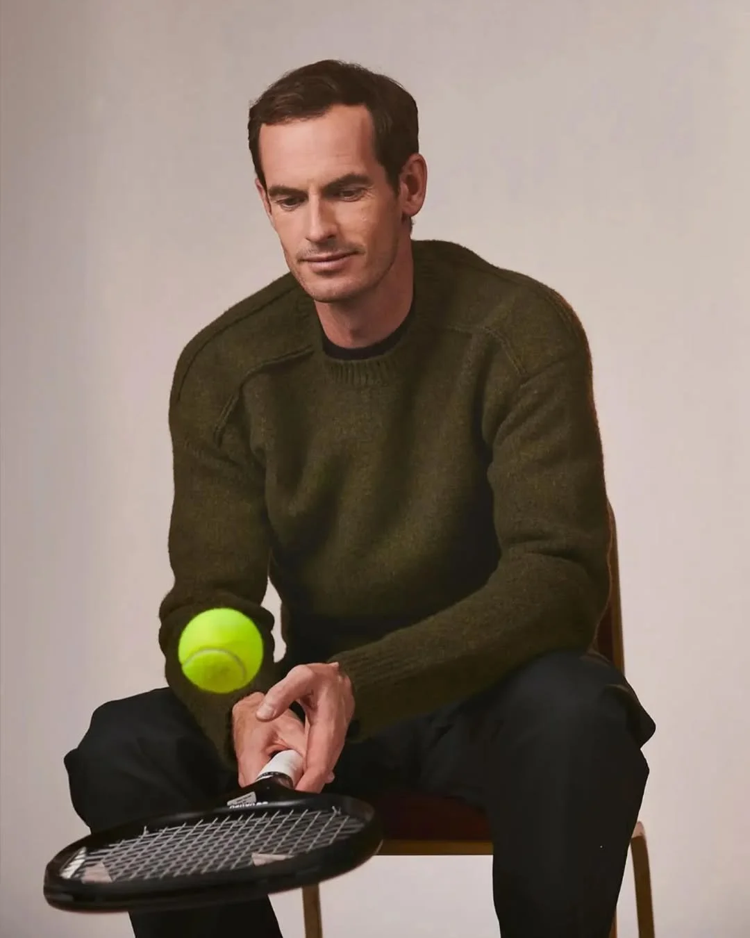 Andy Murray sitting on a chair, holding a tennis racket, with a tennis ball balancing on the racket.