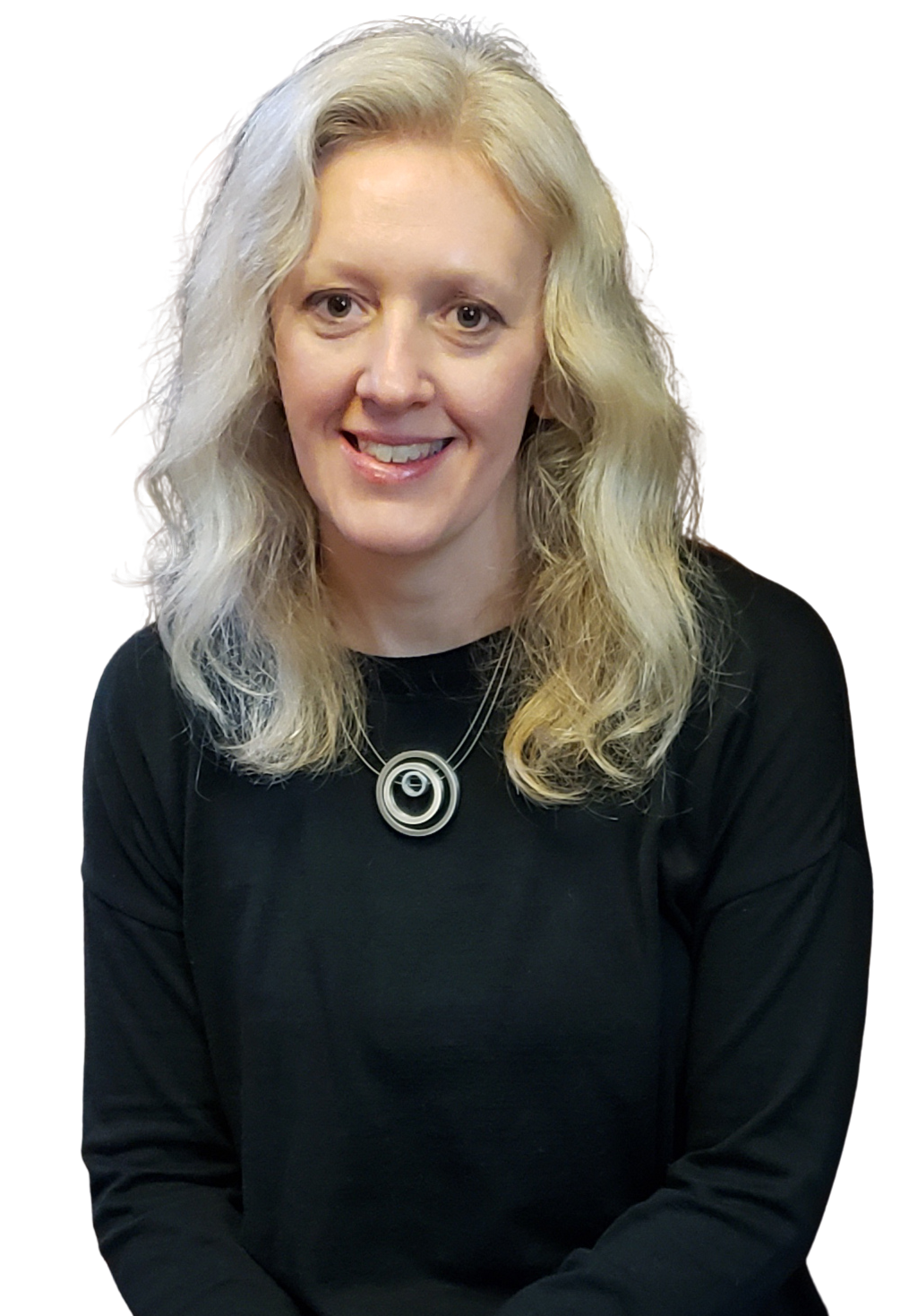 A woman with long, curly blonde hair smiling and wearing a black top and a necklace with a circular pendant.