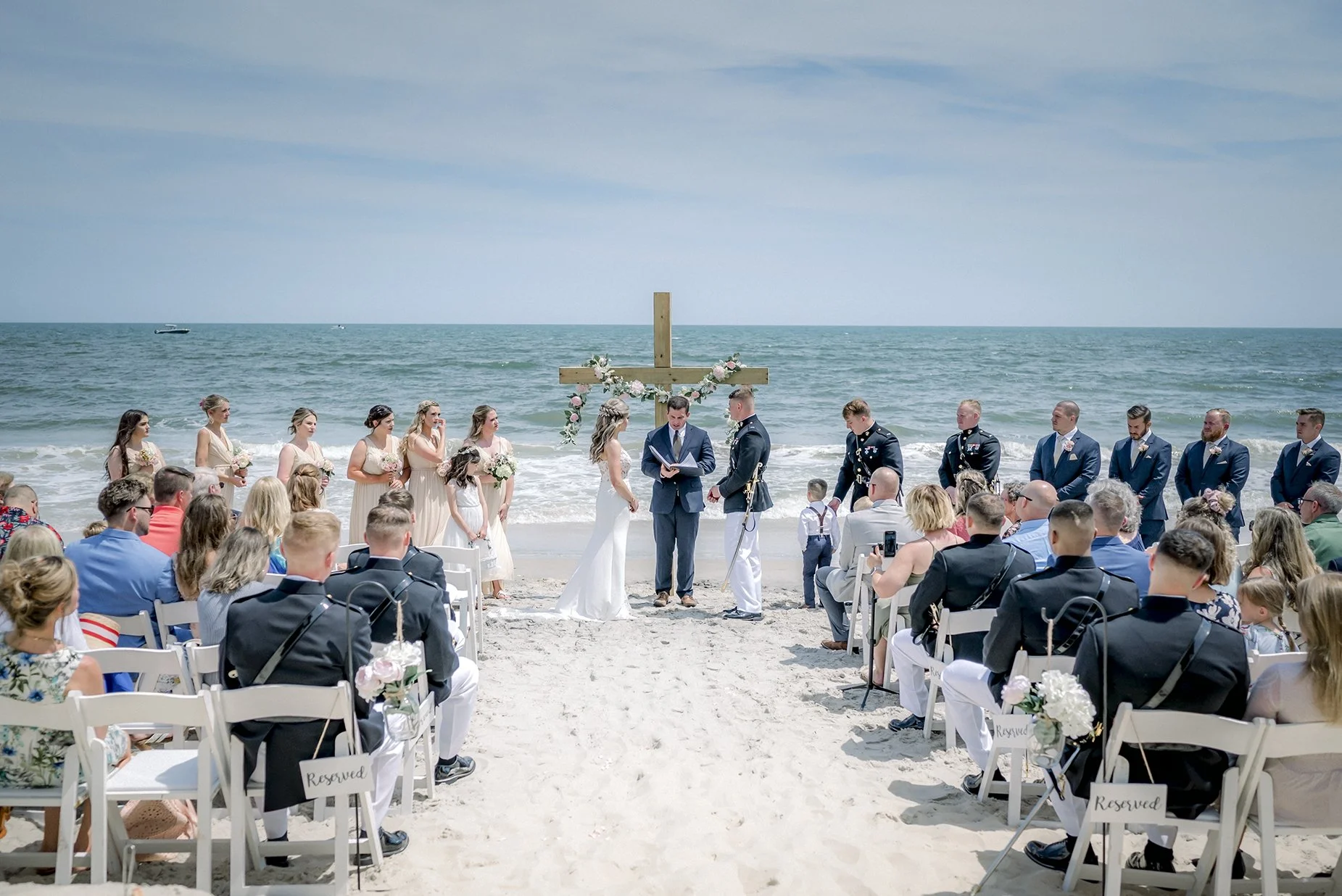 Beach Wedding Ceremony with boat in the Ocean wedding guests and wooden cross altar with flowers
