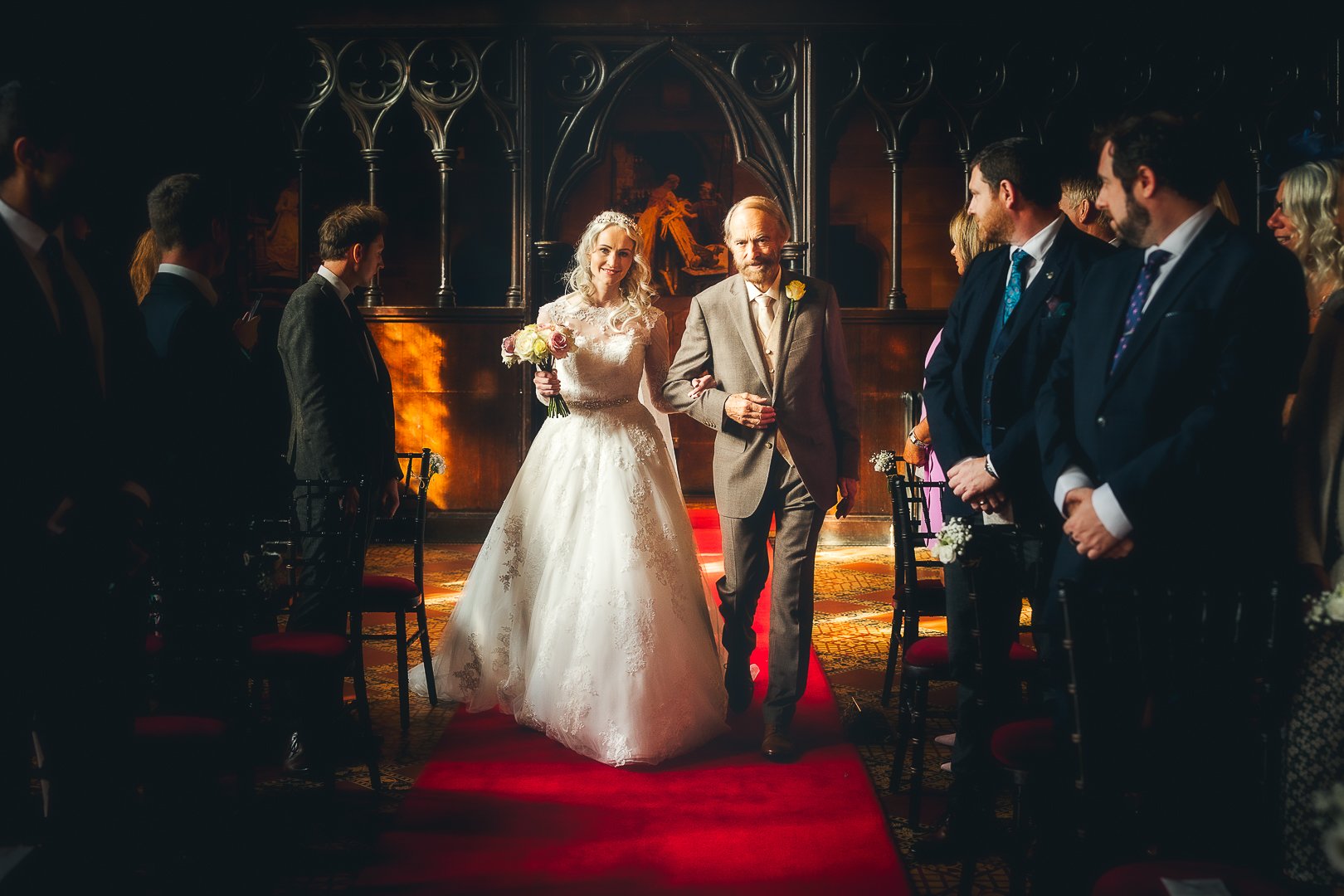 Nel walks down the aisle on her wedding day with proud father of the bride at Peckforton Castle in Cheshire