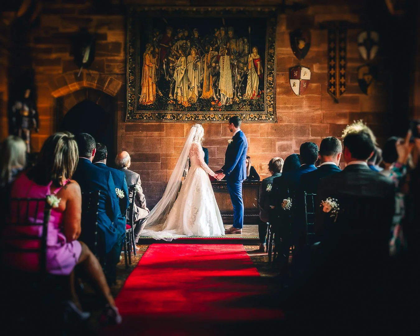 Newlyweds standing hand in hand at the front of the aisle during their wedding ceremony at Peckforton Castle, Cheshire.