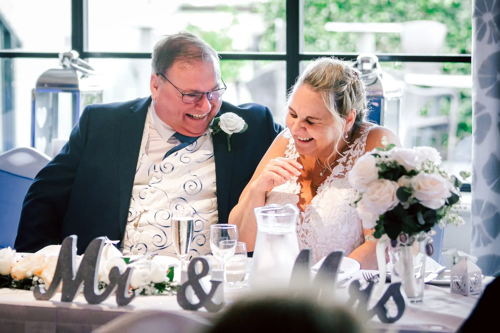 a bride and groom laugh out loud during their wedding breakfast on their big day in Manchester