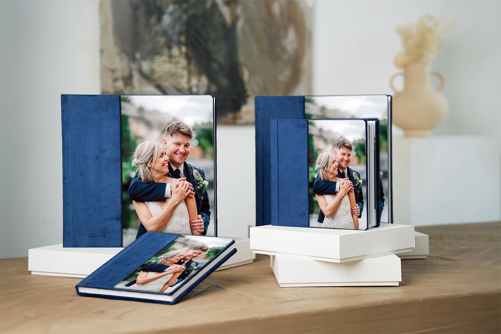 Four wedding photo albums sit in various positions on presentation boxes. The front of the albums are finished in royal blue linen with an acrylic window showing a bride and groom on their wedding day in Manchester
