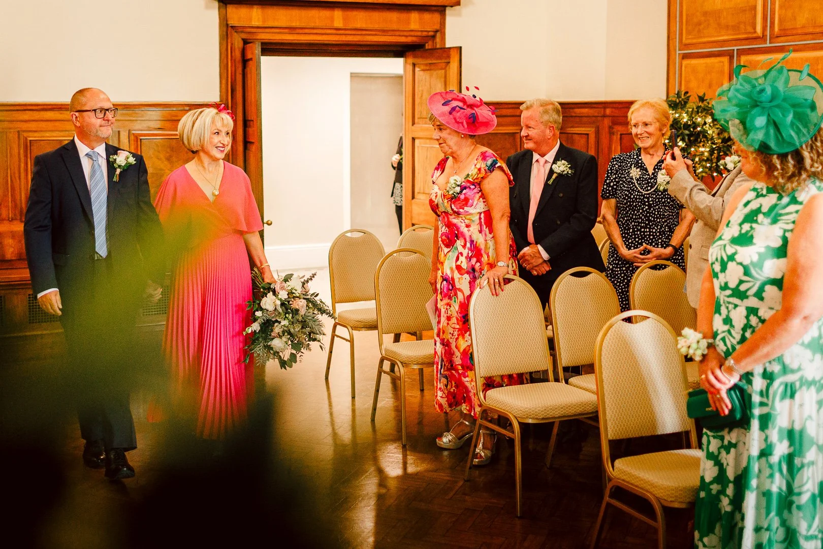 The moment the bride enters the ceremony room in a bright pink dress, walking down the aisle accompanied by her groom at the start of their wedding ceremony, the moment captured by a Sale Town Hall wedding photographer.