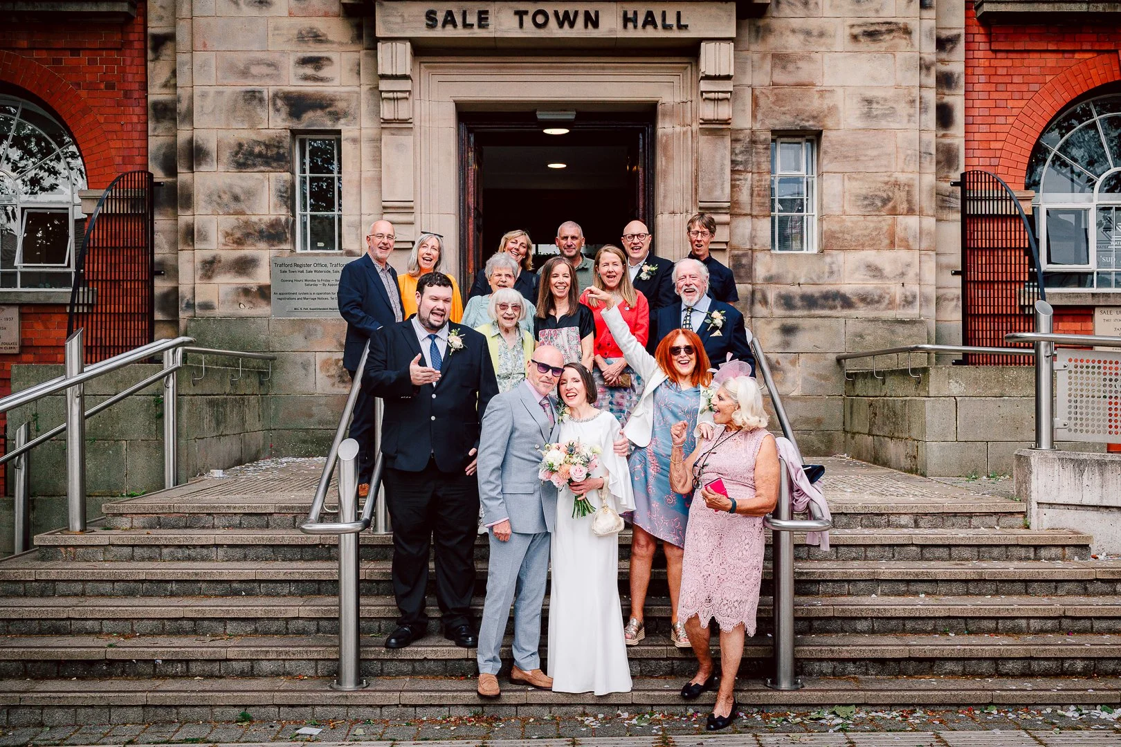 family and friends gather on the steps of Sale Town Hall for a group portrait to celebrate the wedding day of Dave and Alison