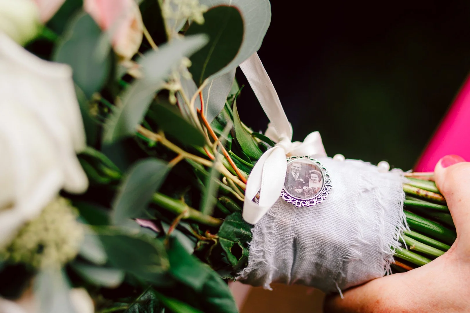 Close-up detail of a white wedding bouquet with a silver memorial charm, styled by a wedding photographer at Sale Town Hall.