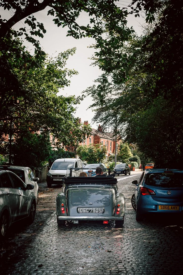 Silver open top Jaguar drives away with newlyweds on board towards their wedding reception