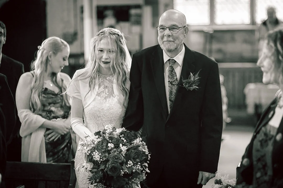 Father of the bride walks his daughter down the aisle on her wedding day inside the cosy Saint Martins Church surrounded by friends family and local residents of Sale