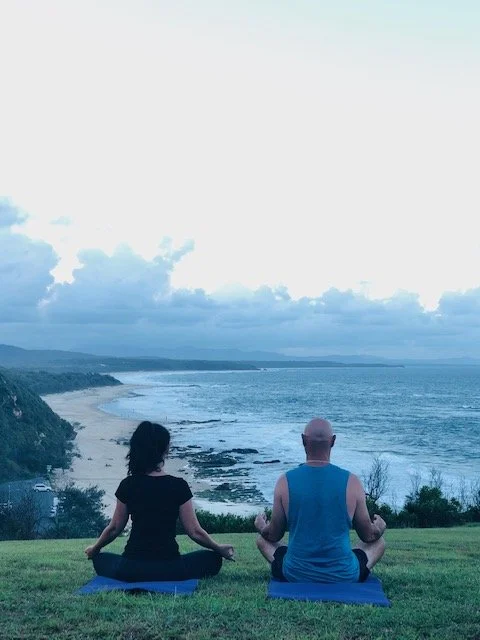 An over 50 couple meditating outside near water