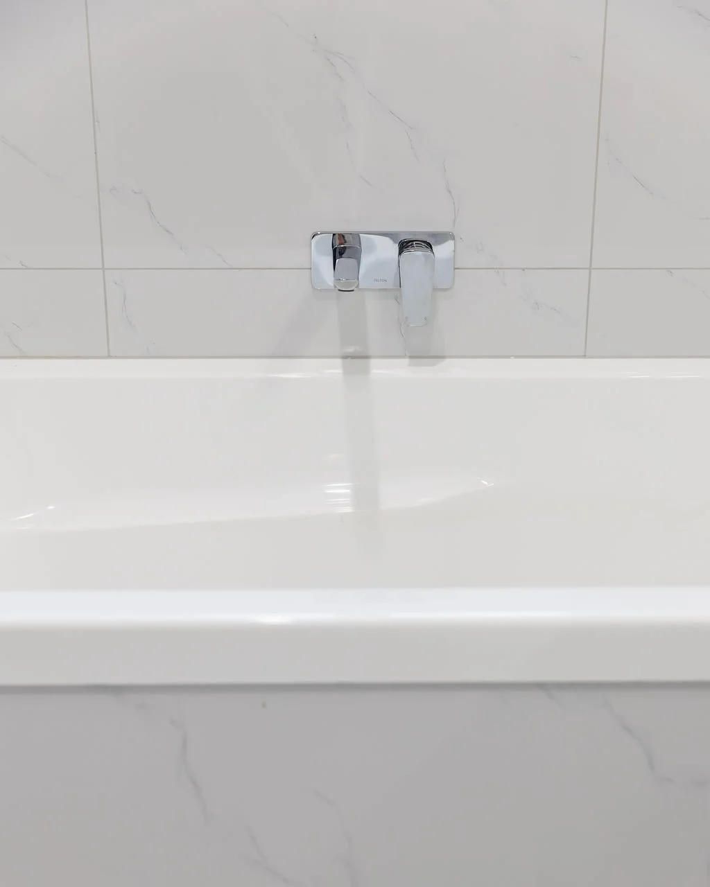Close-up of a wall-mounted chrome bathroom faucet with water running in a white bathtub.