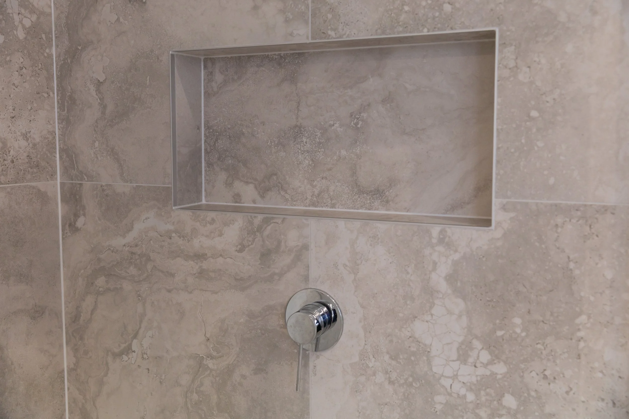 Close-up of a tiled shower wall with a built-in rectangular niche and a chrome shower control knob.