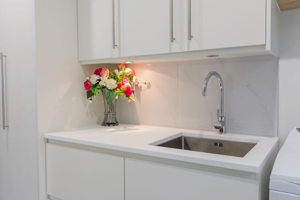 White kitchen with a bouquet of pink and white flowers in a glass vase on the counter, a stainless steel sink, and white cabinets.
