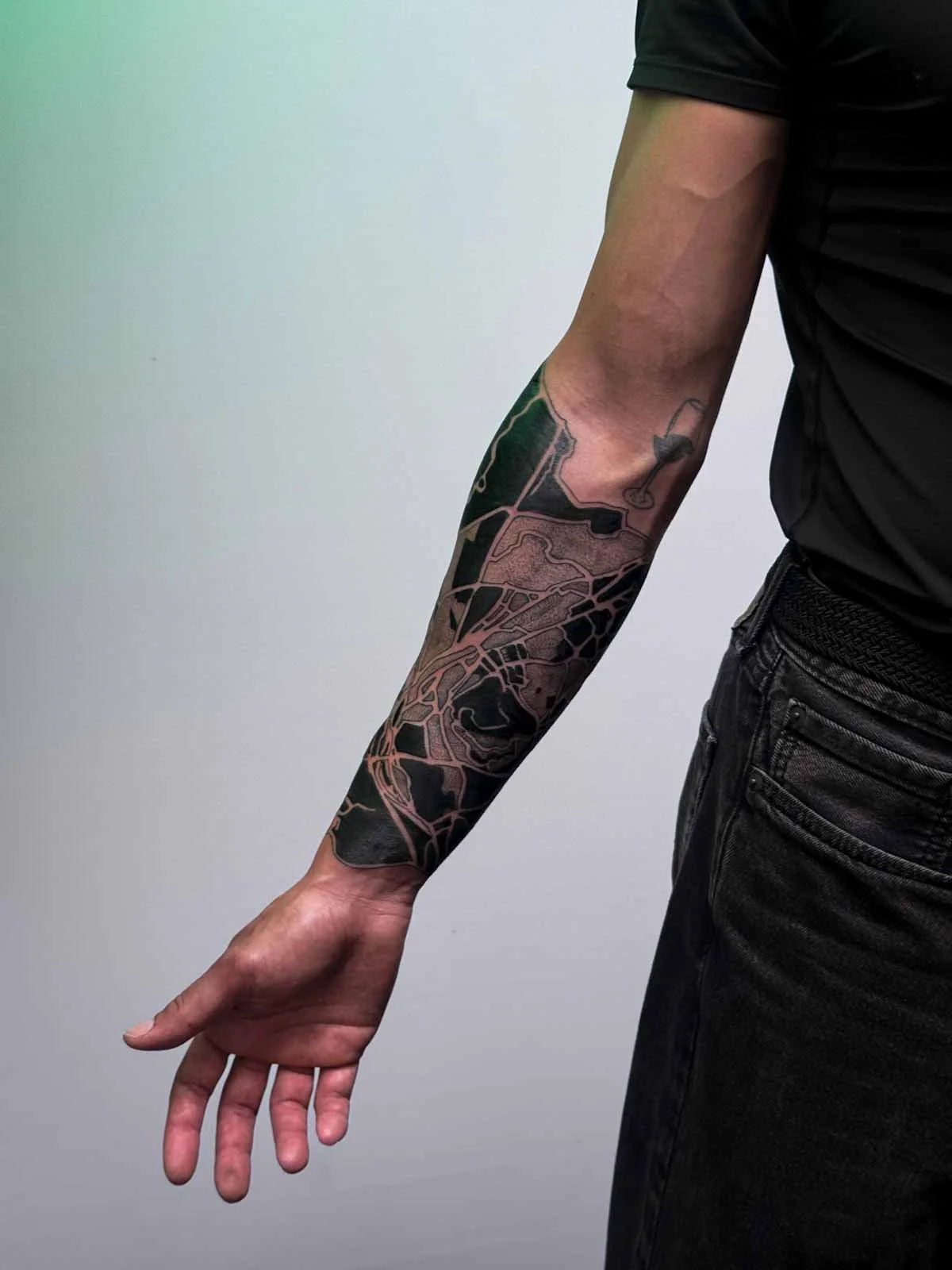 A person with a tattooed right arm of a map of Cairo, Egypt extended downward, wearing a black shirt and black jeans, against a plain light background.