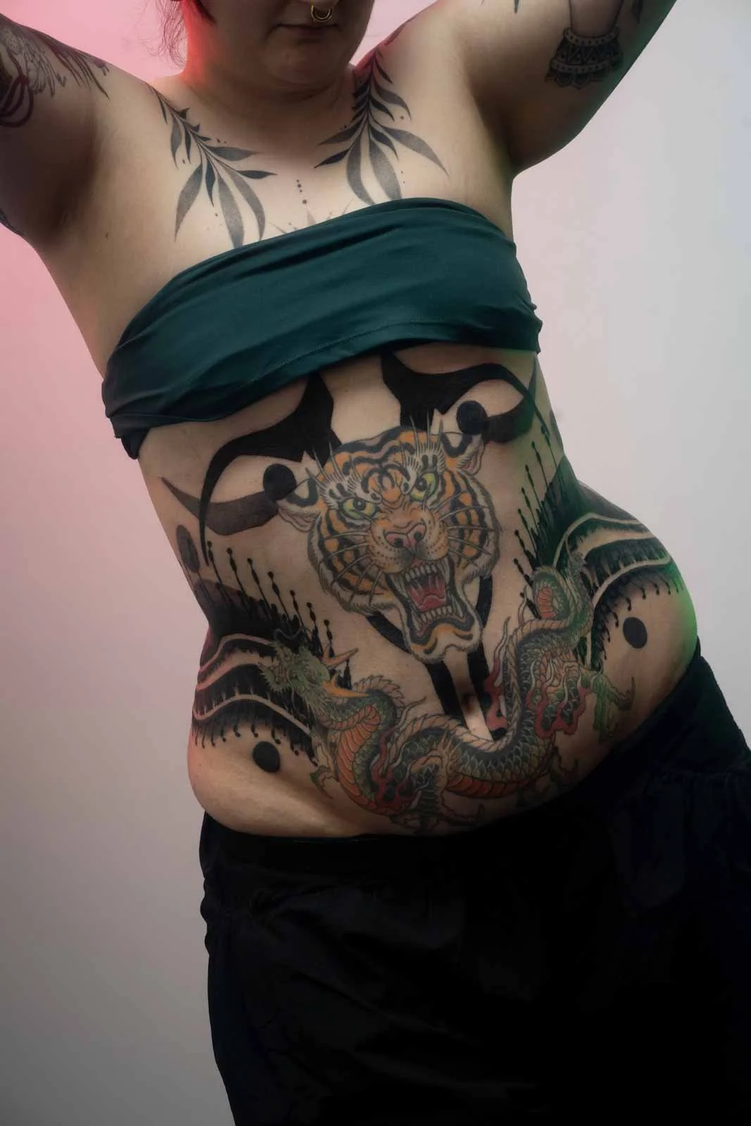A person with tattoos exposing their tattoos on the stomach and chest, including a tiger and a snake, while holding their arms up.