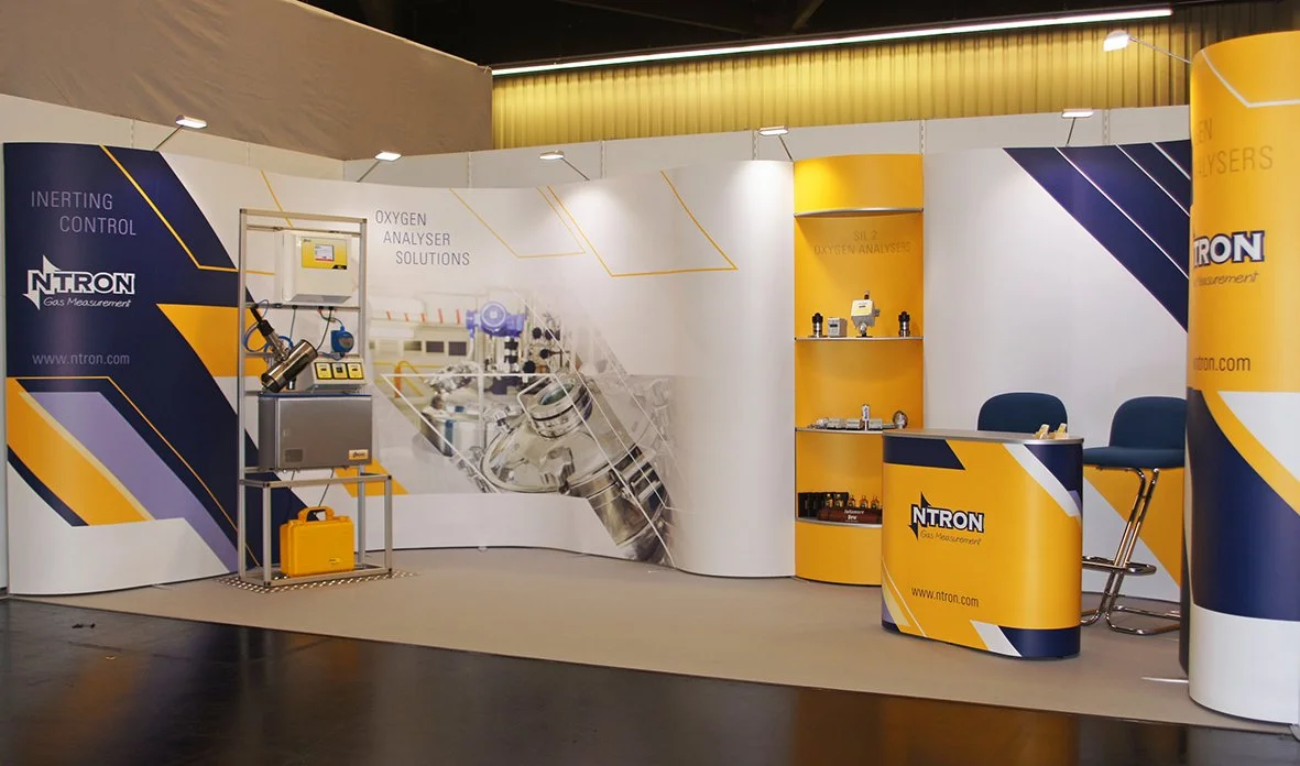 Trade show booth for NTRON Gas Measurement featuring equipment and promotional materials in blue, yellow, and white colors.