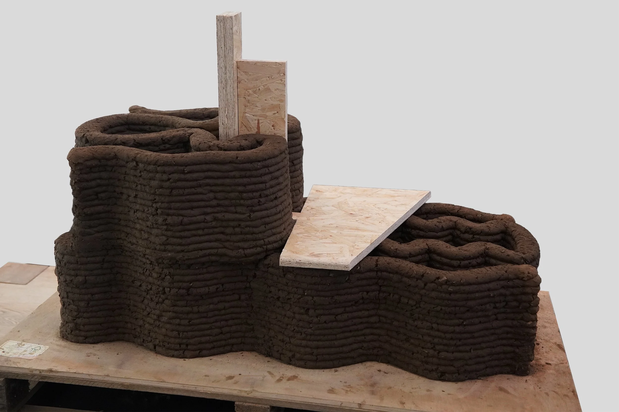 Full-scale 3DPE prototype demonstrating wall geometry with embedded OSB floor plate and timber post, showing the integration of structural timber elements within the printed earth wall during and after printing. Image: Ben Scott.