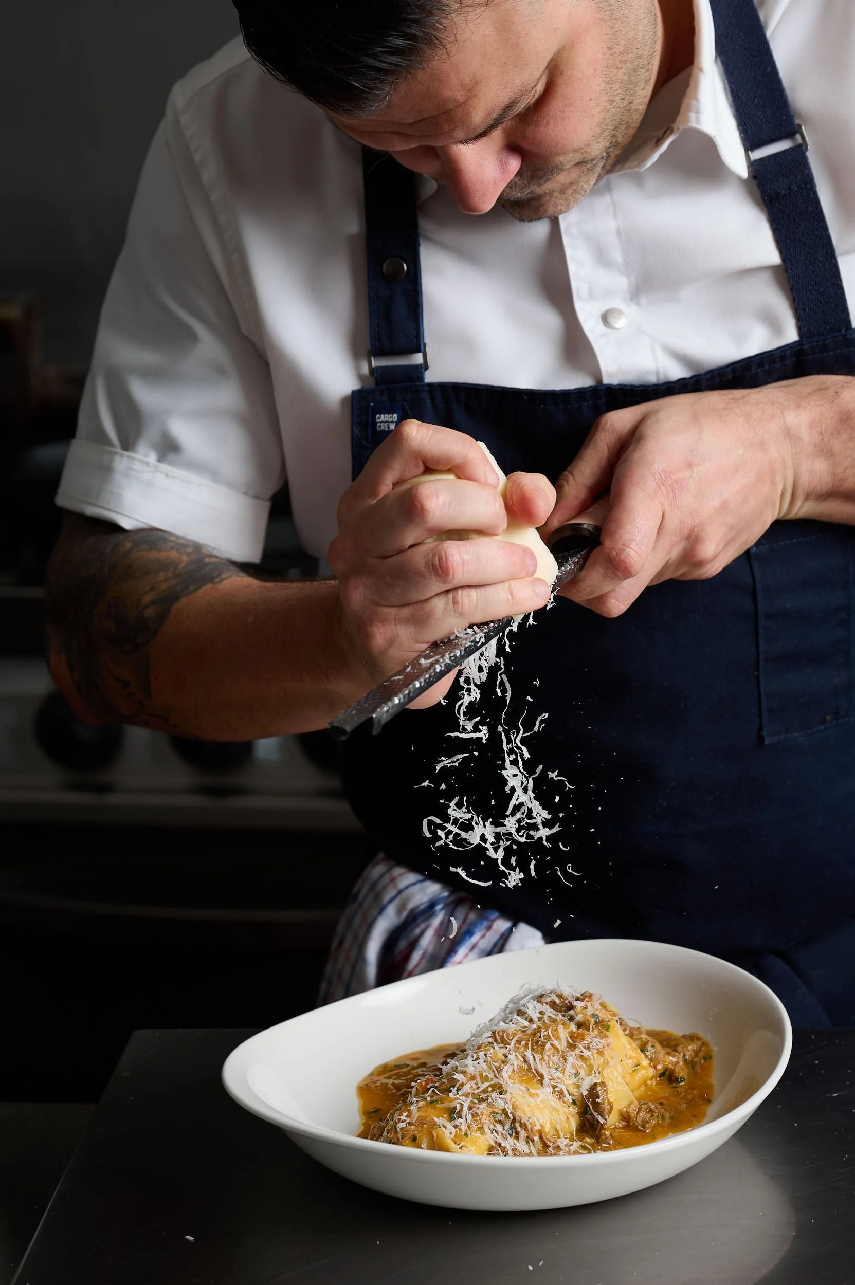Beautiful hospitality photography: restaurant chef grating cheese onto pasta by Charlotte Orr, photographer based in Melbourne, Australia