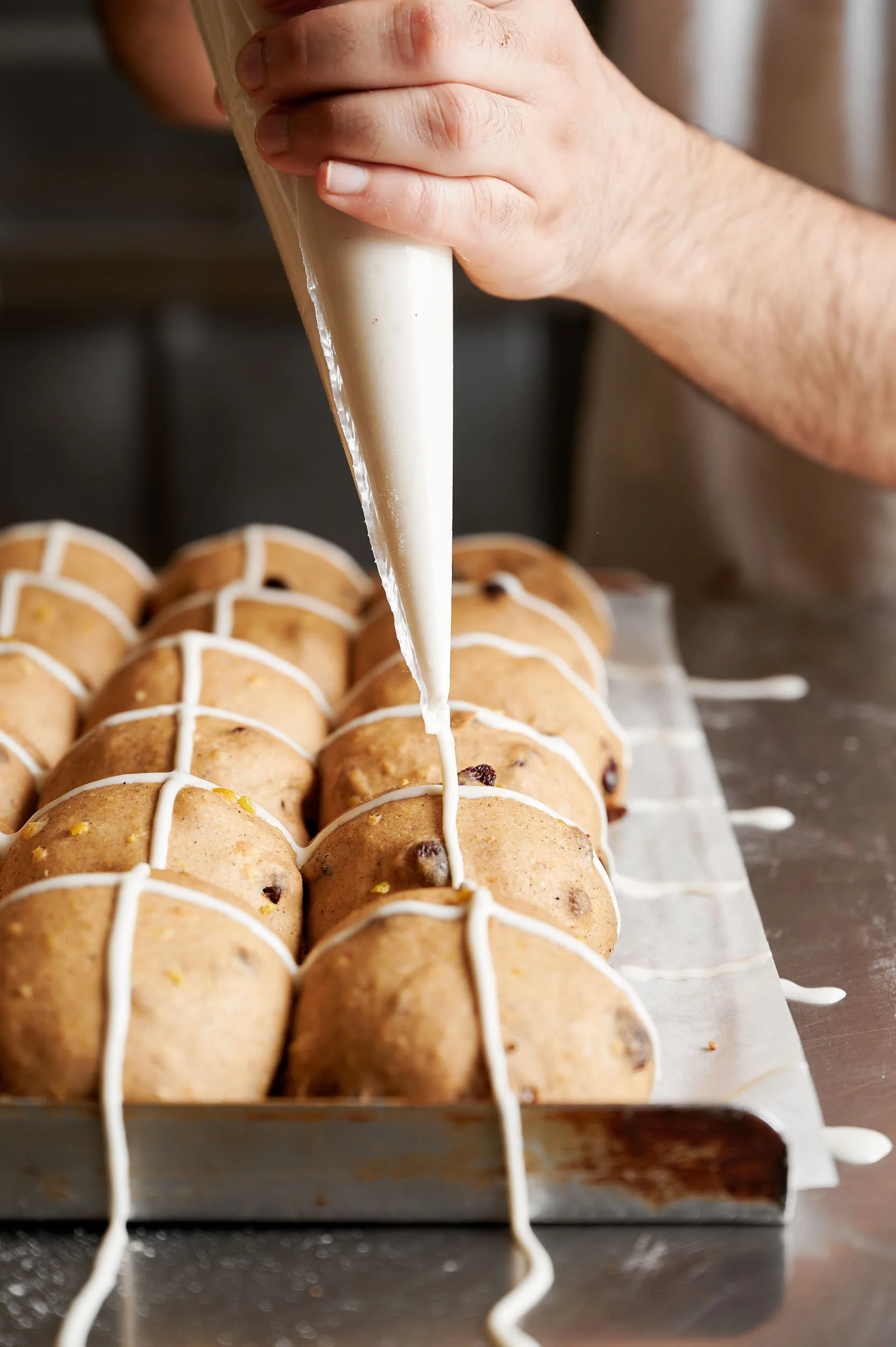 Editorial food photography: hands piping 'cross' onto hot cross buns by Melbourne food photographer Charlotte Orr