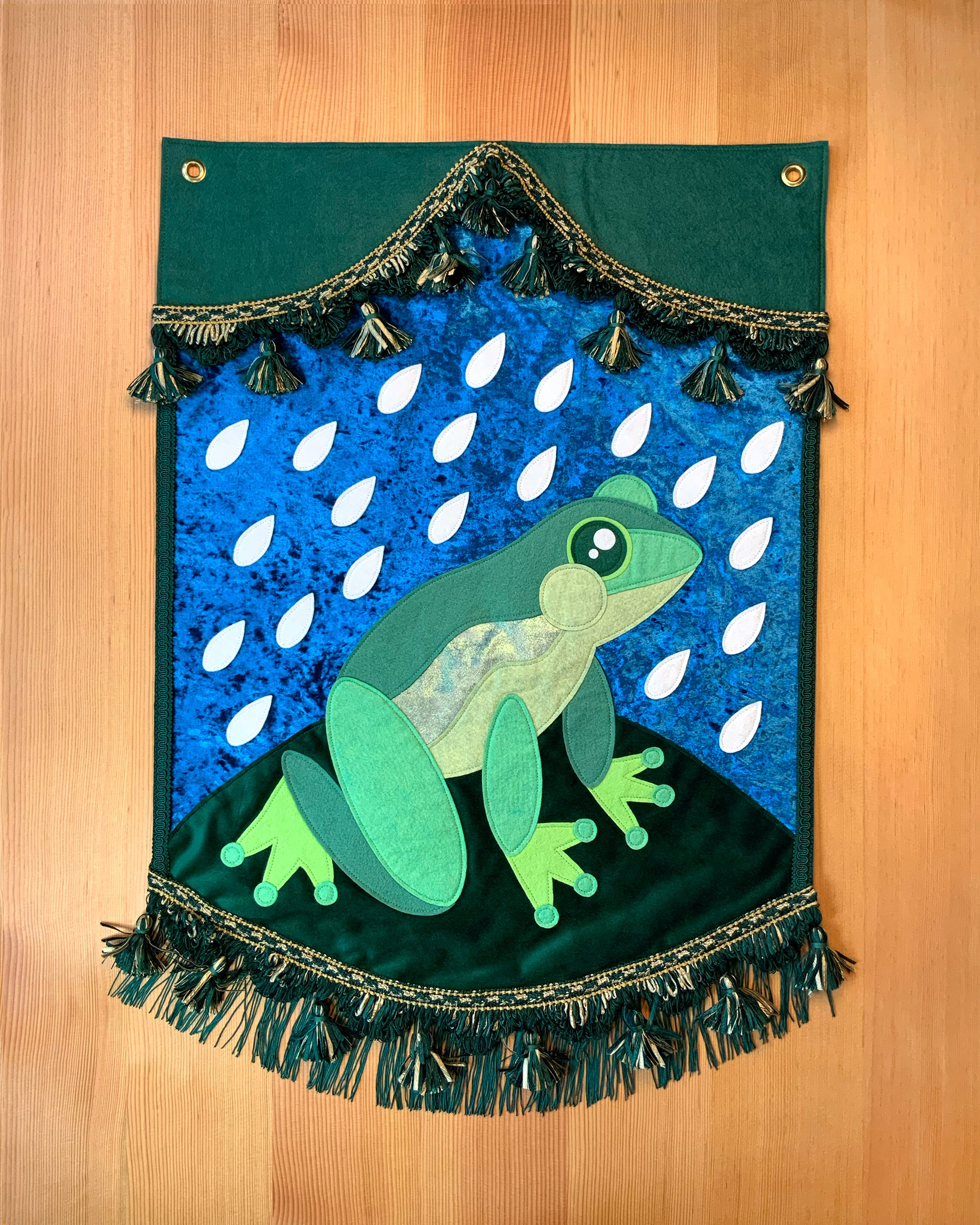 "Sweet Frog in the Rain" (2025) wool-blend felt, velvet, fringe & tassel trim, thread, brass grommets, 22”x32”
