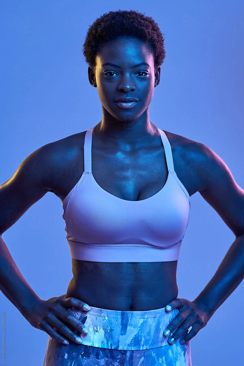 Team Member Teshia Harris stands with hands on hips against purple background.