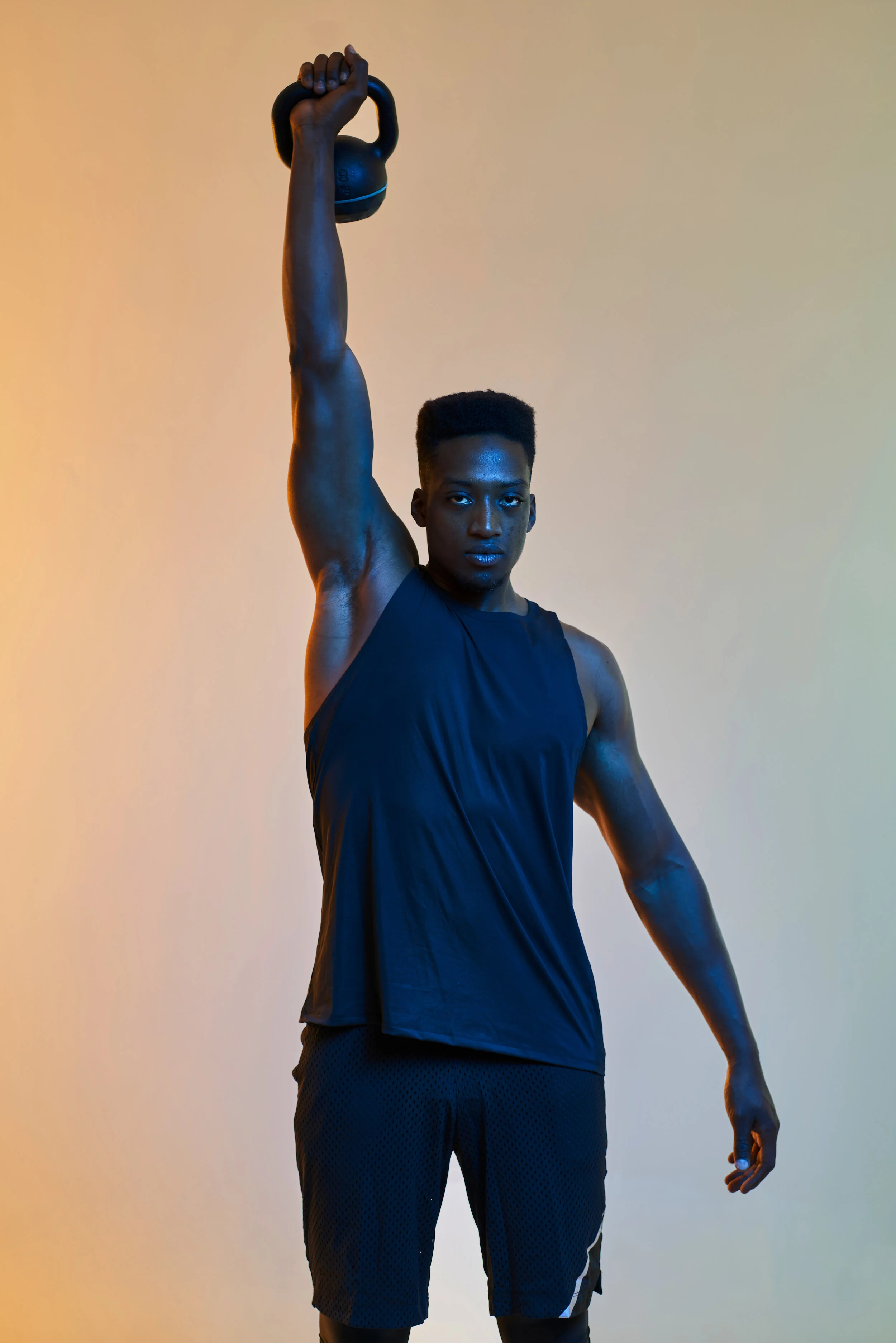 Team Member Aaron Hughes stands with kettle bell lifted over head on gradient background