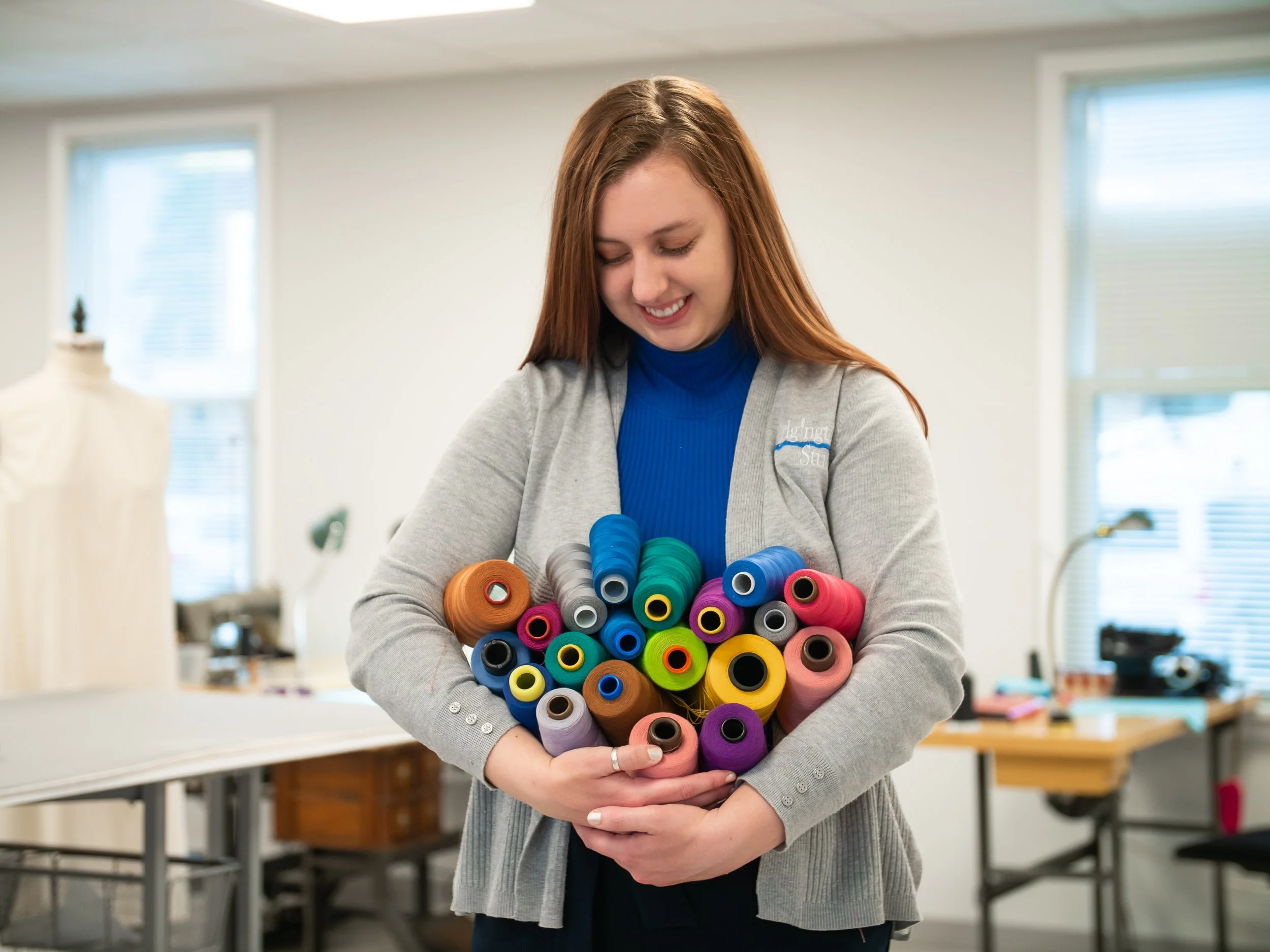 Portrait of Emily Rouse cradling a stack of colorful thread.