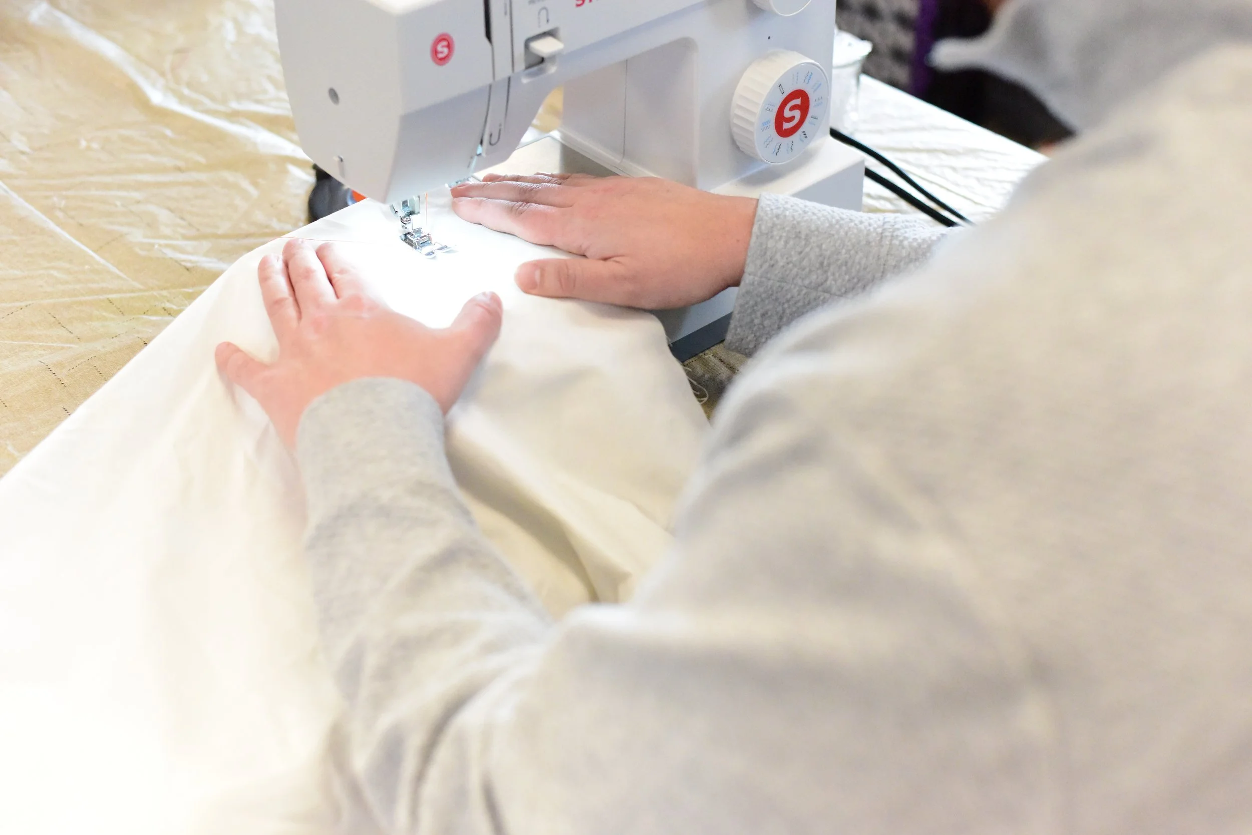 Over the shoulder perspective of hands guiding fabric through a class sewing machine.