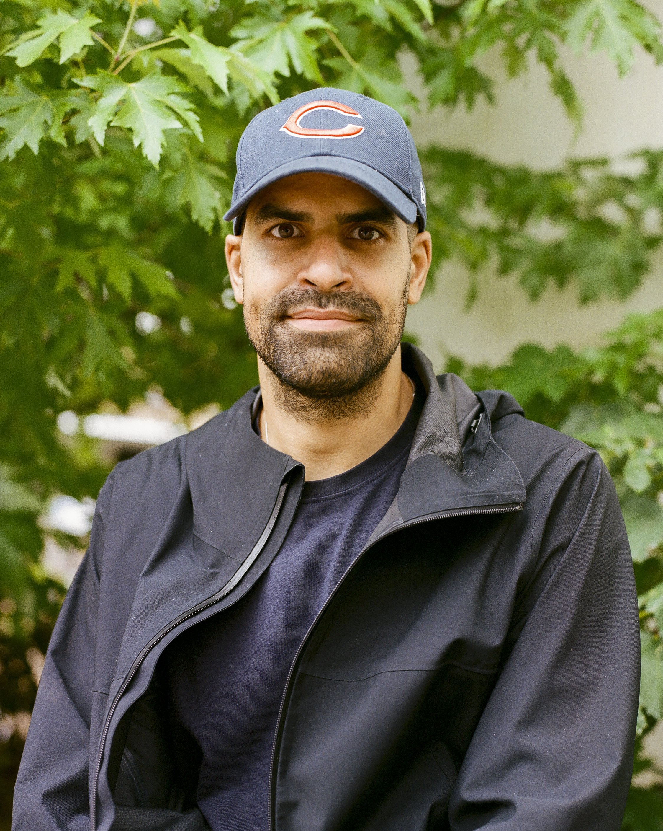 Phil Dobson, founder of upCYCLE LDN, standing outdoors in front of a leafy green bush, smiling at the camera.