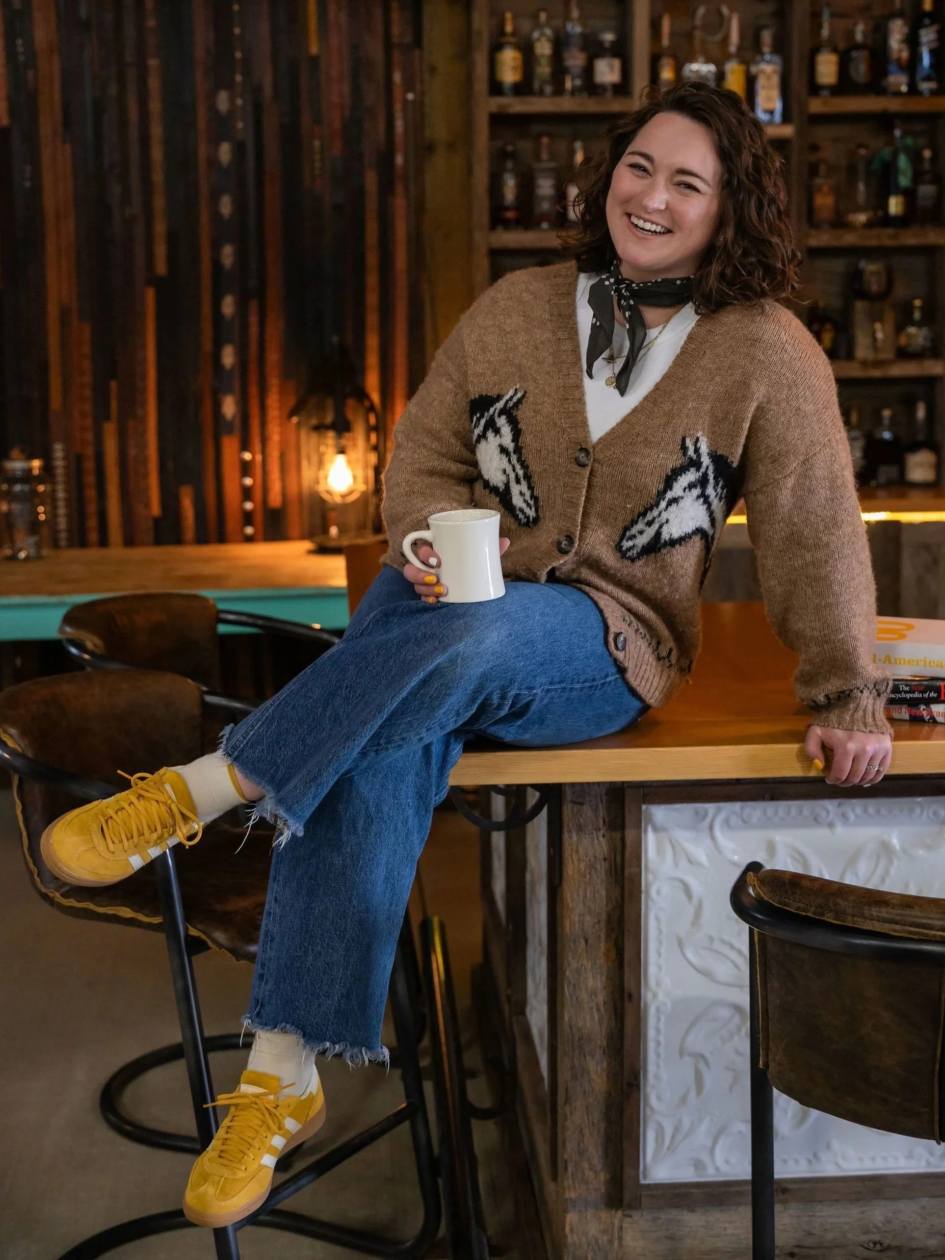 Taylor, owner and lead strategist of Hay&Co. Holding a coffee, wearing a horse sweater and signature yellow shoes. Photo by Shelly Borga