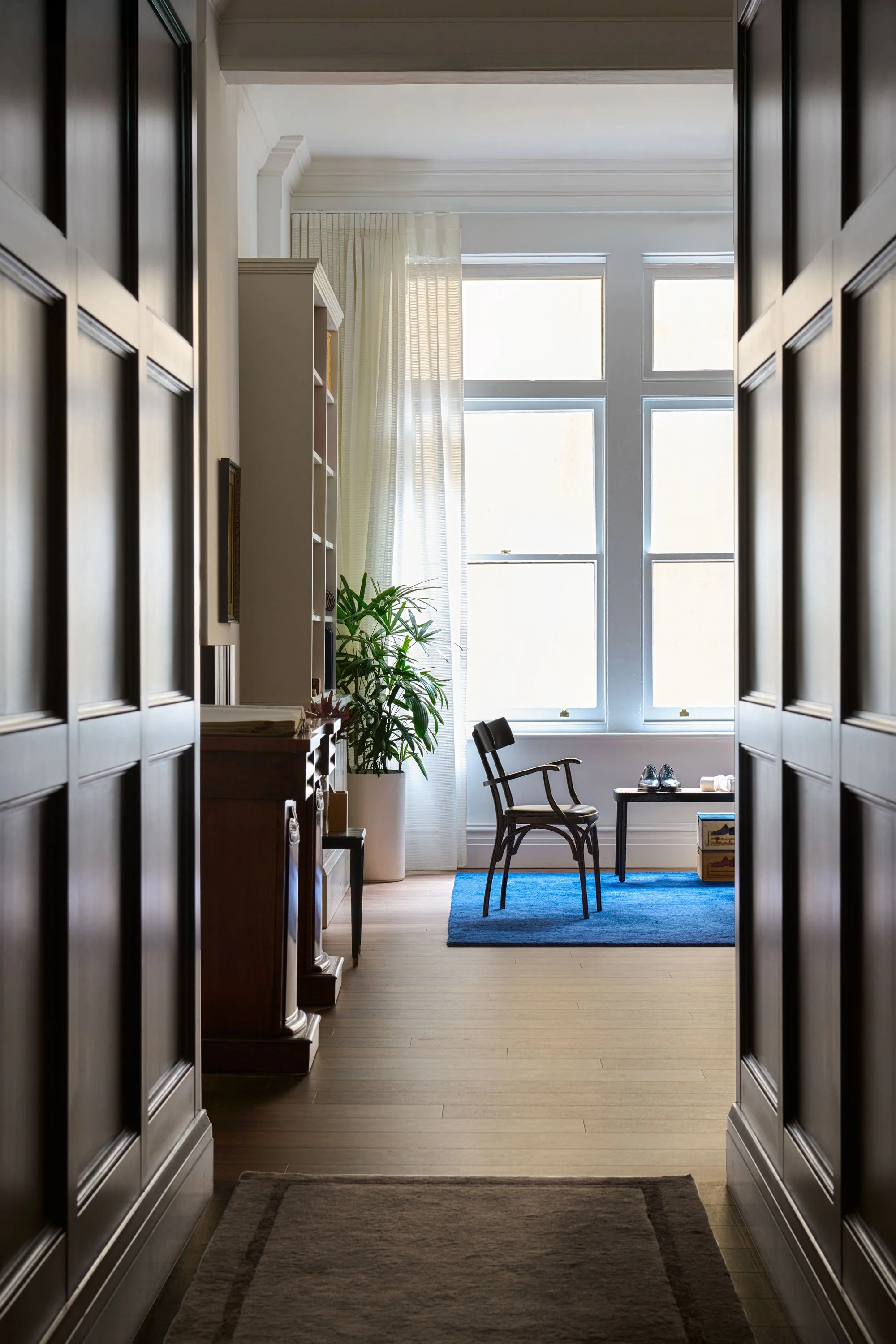 Perspective view through the timber-panelled hallway at J.H. Cutler’s atelier leading to a bright client seating area with classic furniture.