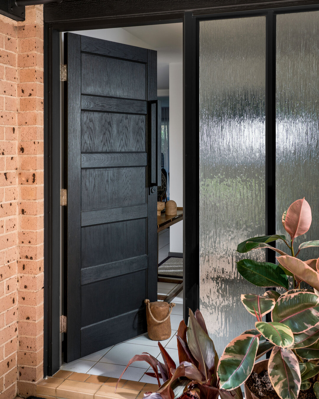 PORT STEPHENS HOUSE II - the journey begins at the striking entry door. Crafted from solid timber with an open grain and stained black, it exudes a sense of timeless beauty and grandeur. As you pass through the door, the foyer opens up, revealing a b