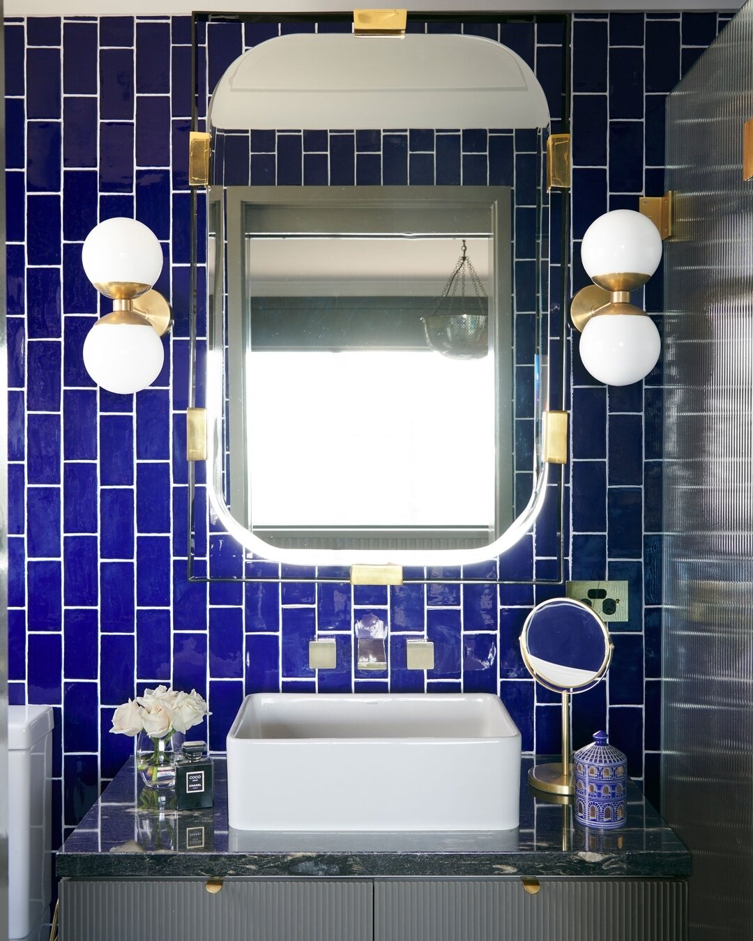 PORT STEPHENS HOUSE I - Cobalt wall tiles create a bold and captivating backdrop, infusing the space with a vibrant energy. A brass and iron mirror adds a touch of elegance with quartzite benchtops below. Statement wall lights provide both ambient an