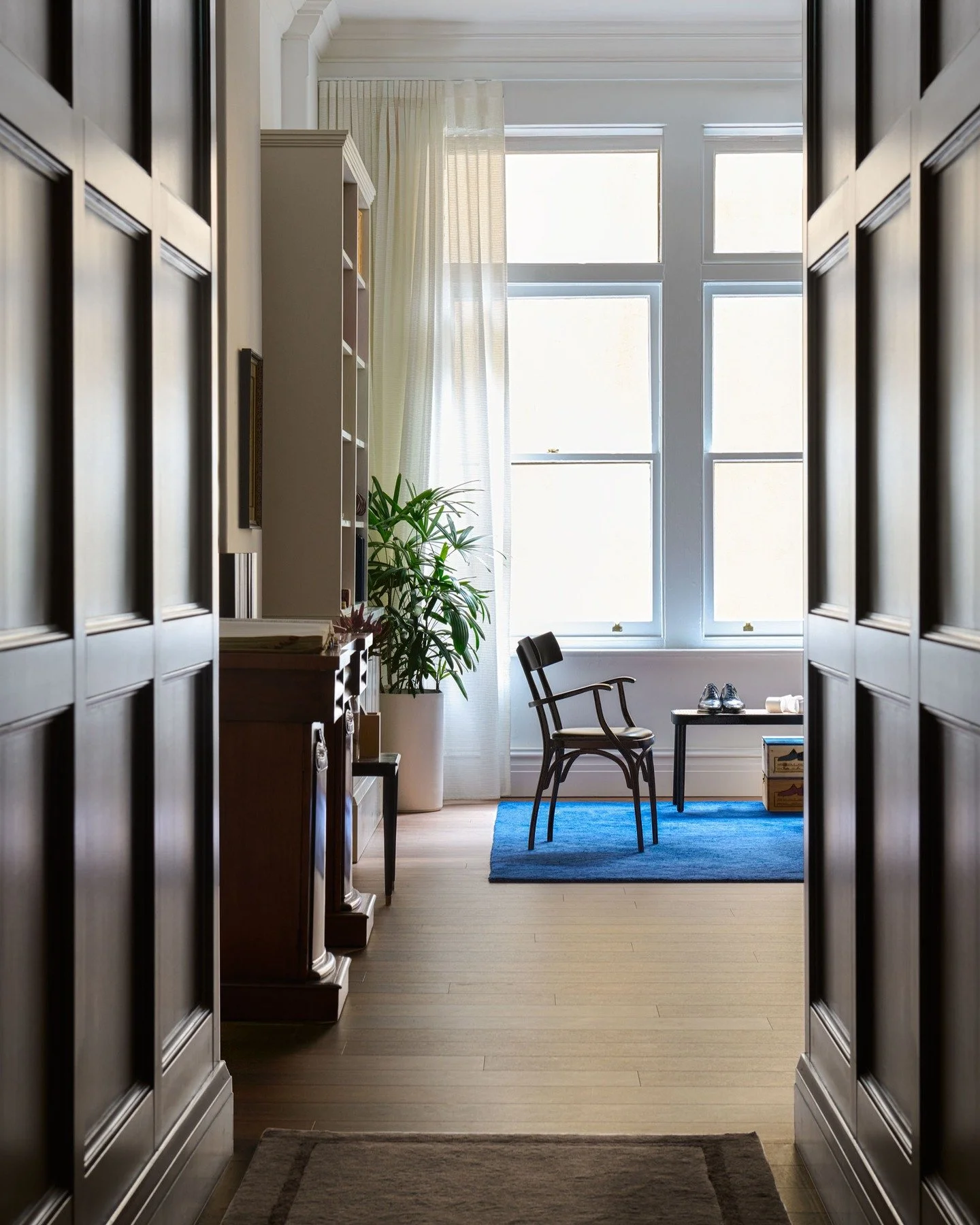 J H CUTLER - Timber panelling frames the approach to a light-filled showroom at J.H. Cutler. Daylight filters through sheer curtains onto the timber floors and a cobalt rug, where a single chair and table sit ready for fittings. A space defined by pr