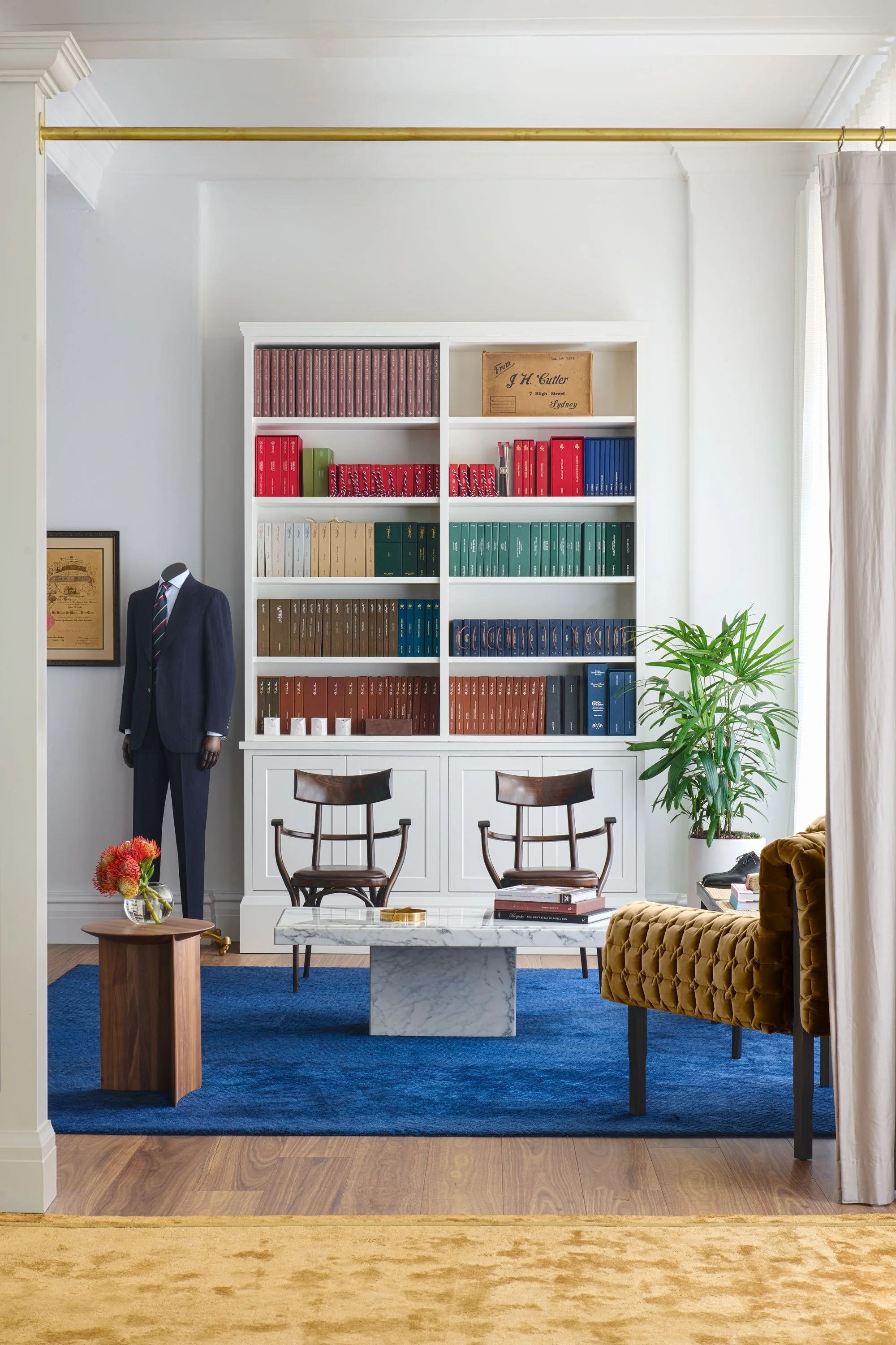 Full wall view of bespoke fabric books in a classic white joinery setting with mid-century chairs and marble table at J.H. Cutler Sydney showroom.