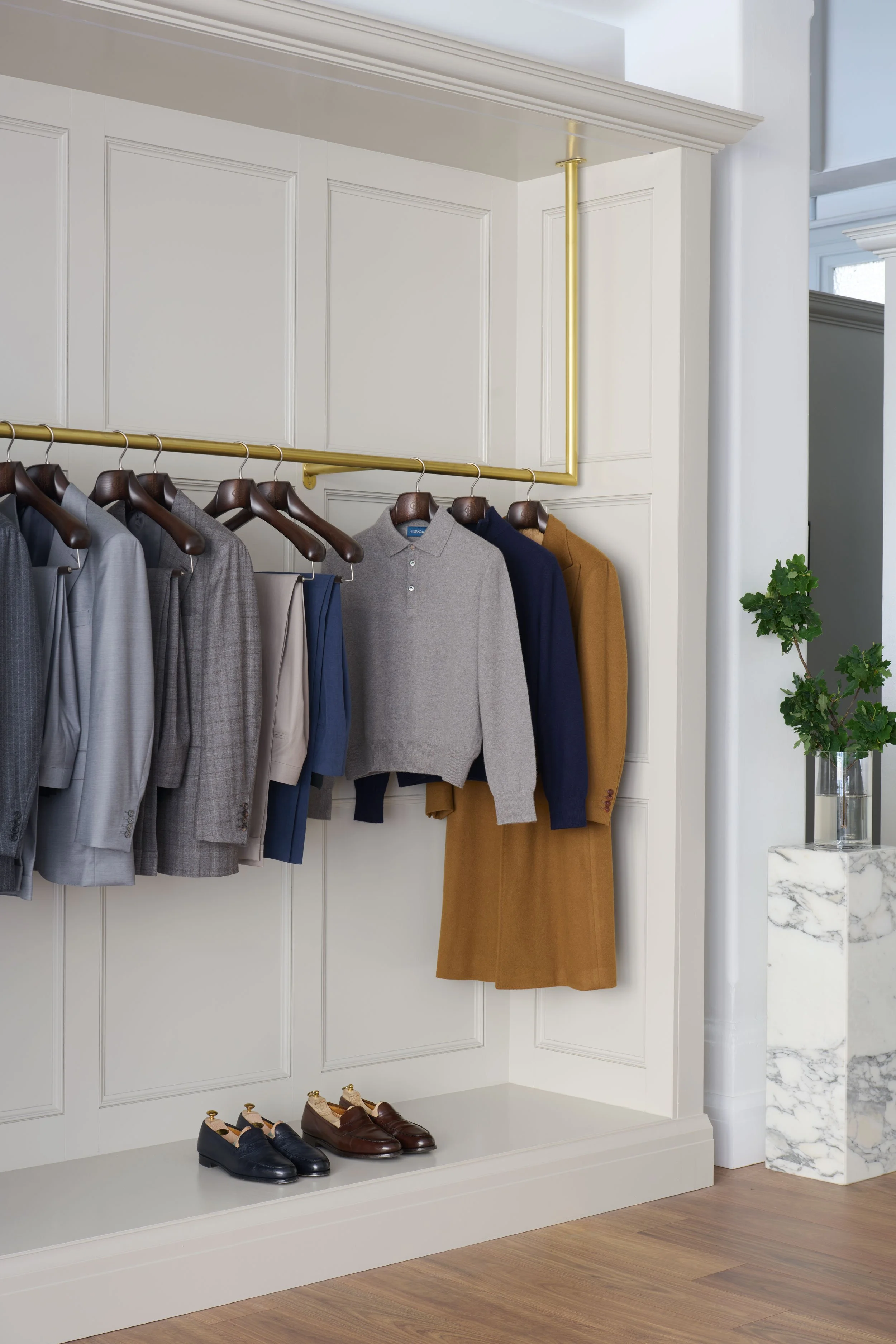 Curated rail with tailored jackets, wool overcoats, and handmade leather shoes beneath brass hanging rod at Sydney’s J.H. Cutler atelier.