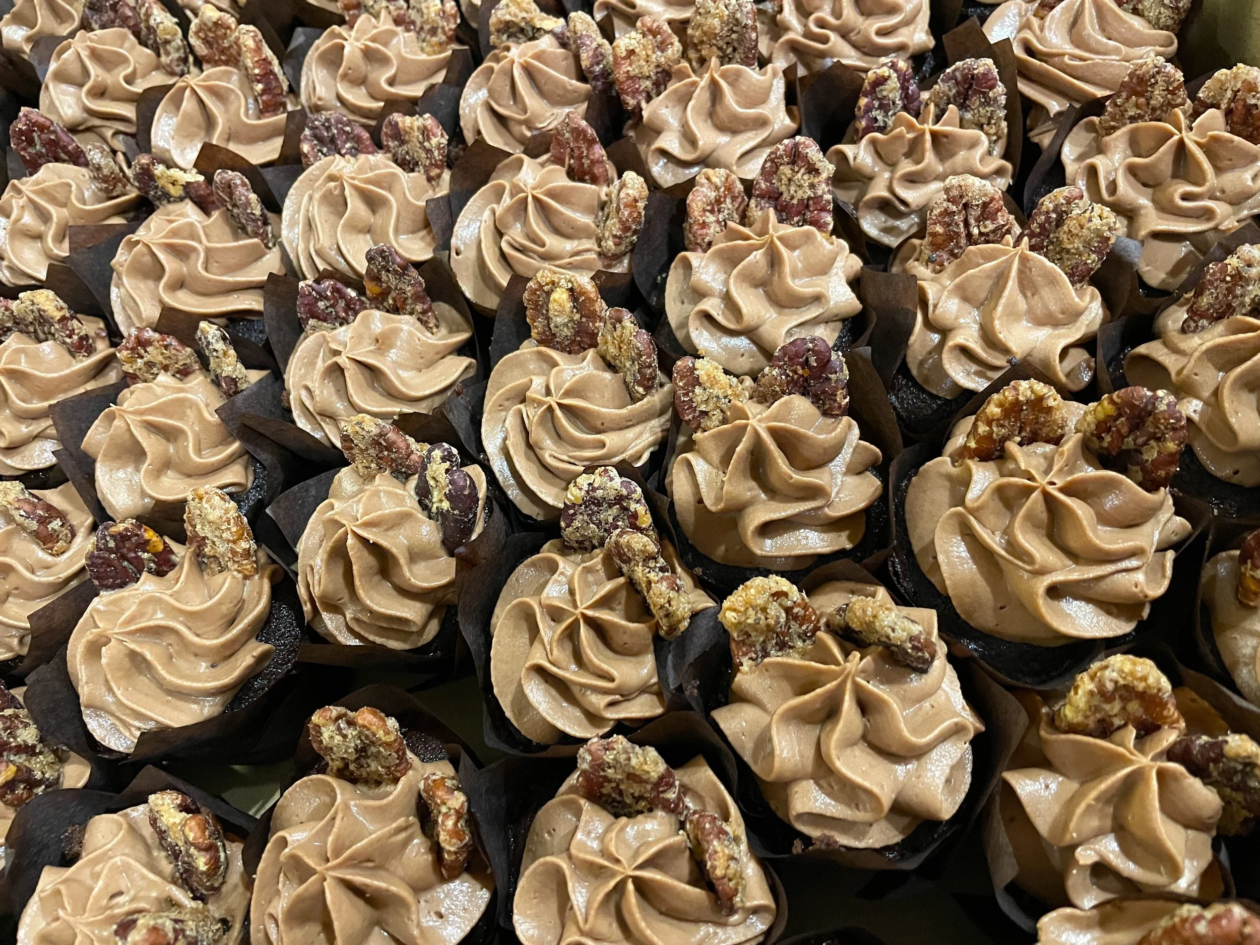 tray of chocolate cupcakes with whipped chocolate ganache and pecan garnish