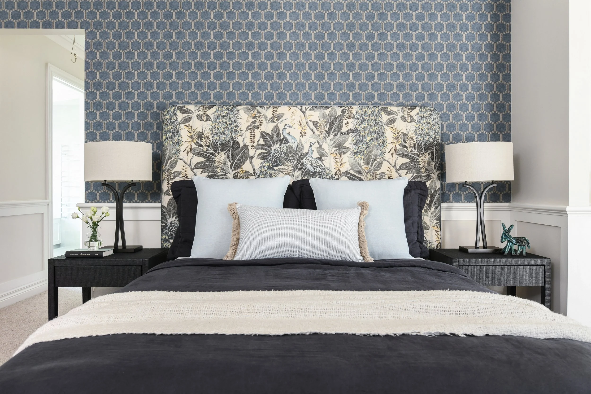 Classic master bedroom with custom headboard, blue wallpaper and grasscloth covered bedside tables